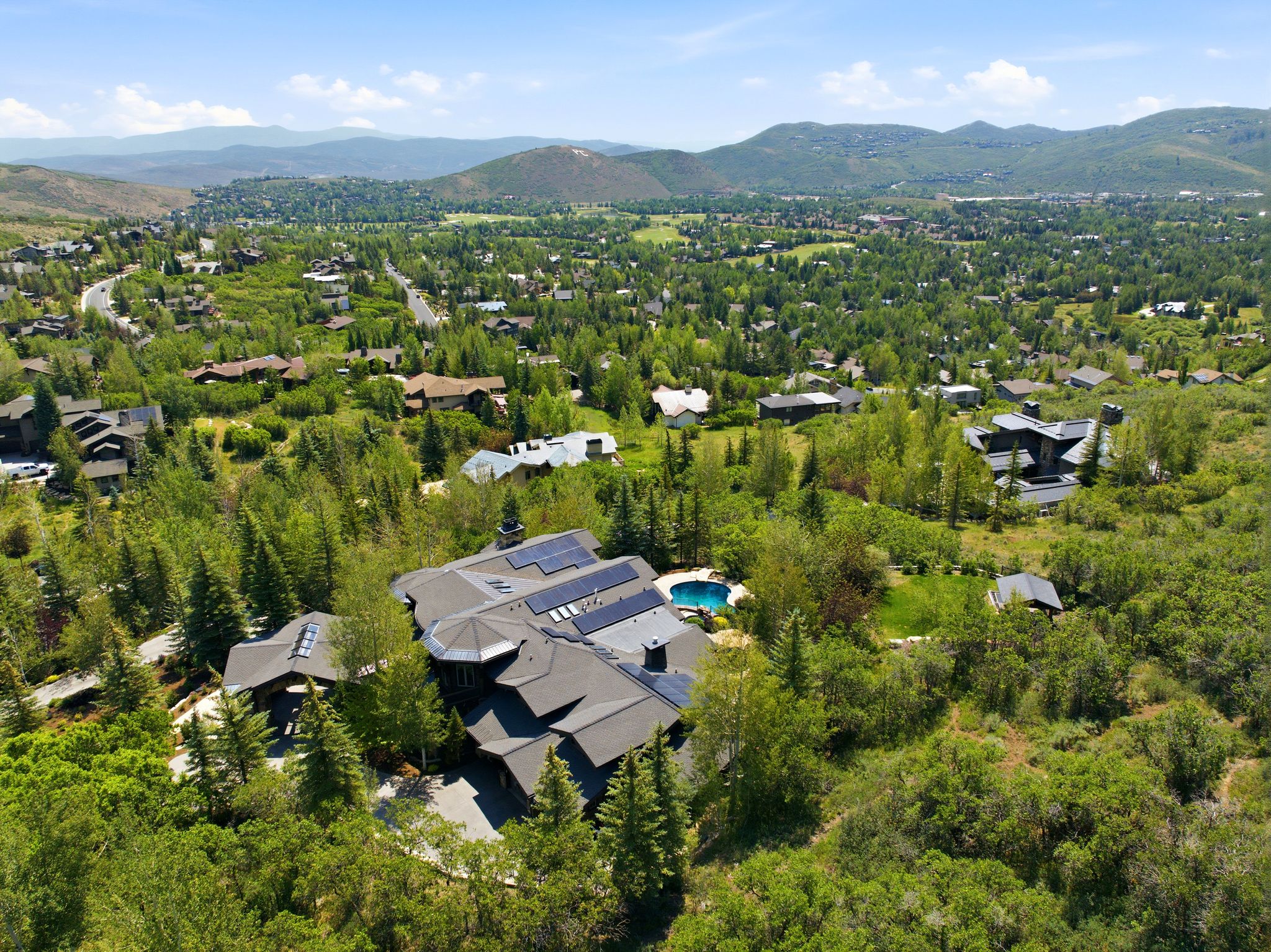 Expansive property featuring a multi-level roofline, integrated solar panels, and a blue-tiled swimming pool