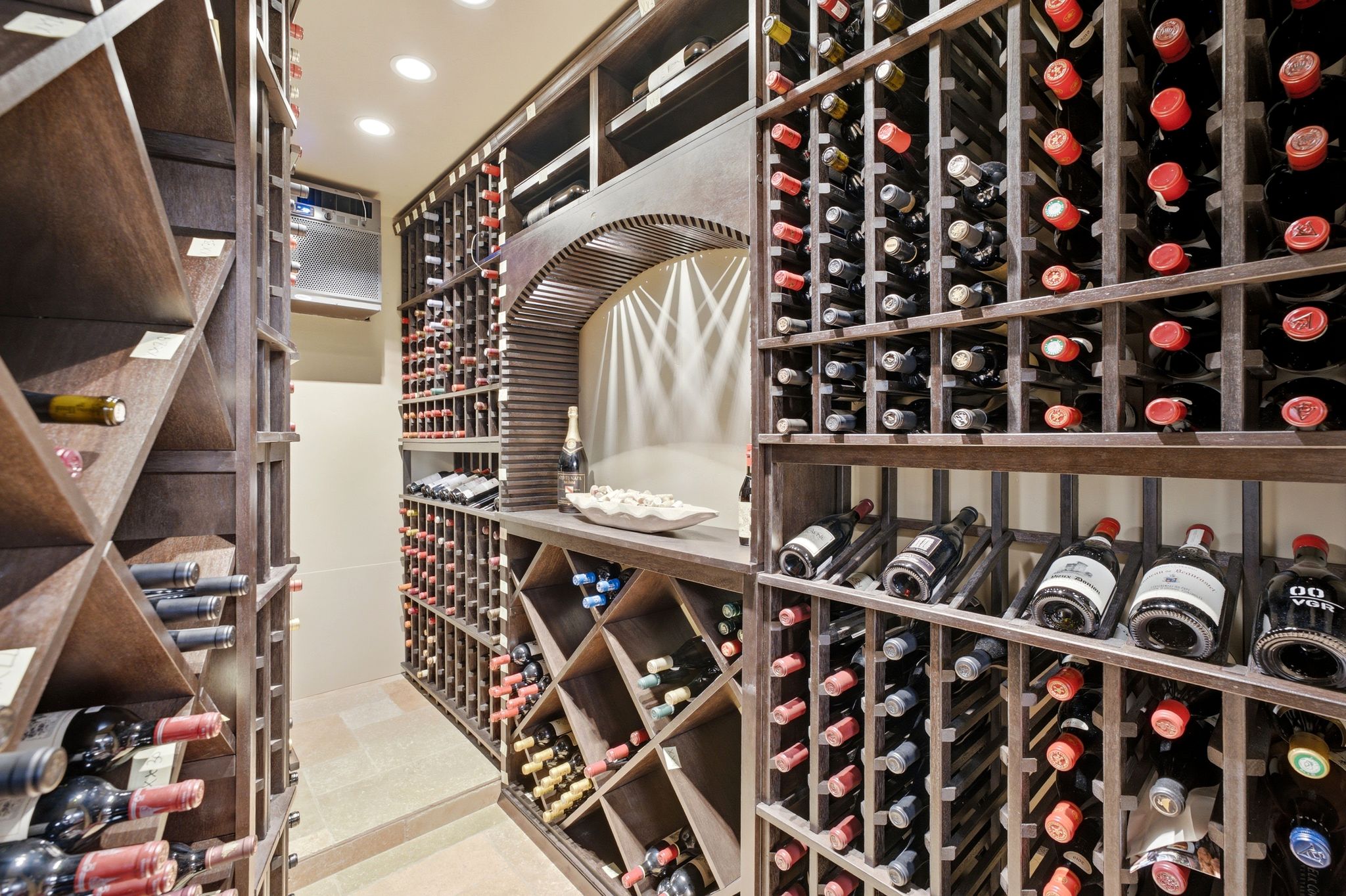 Dedicated wine cellar featuring extensive wood-finish bottle storage, recessed ceiling lighting, a curved arched niche, and tile flooring
