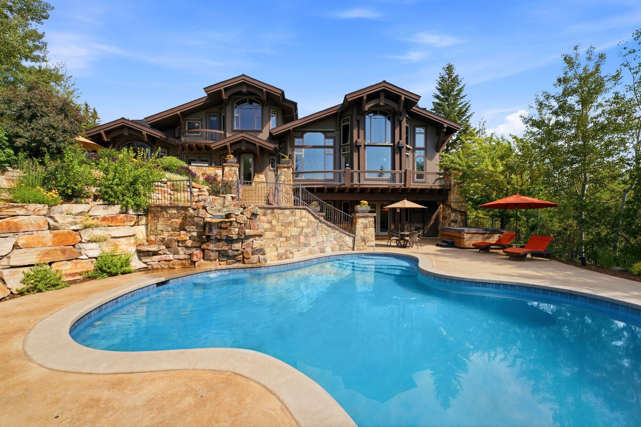 Curved swimming pool with a stone retaining wall and integrated waterfall feature