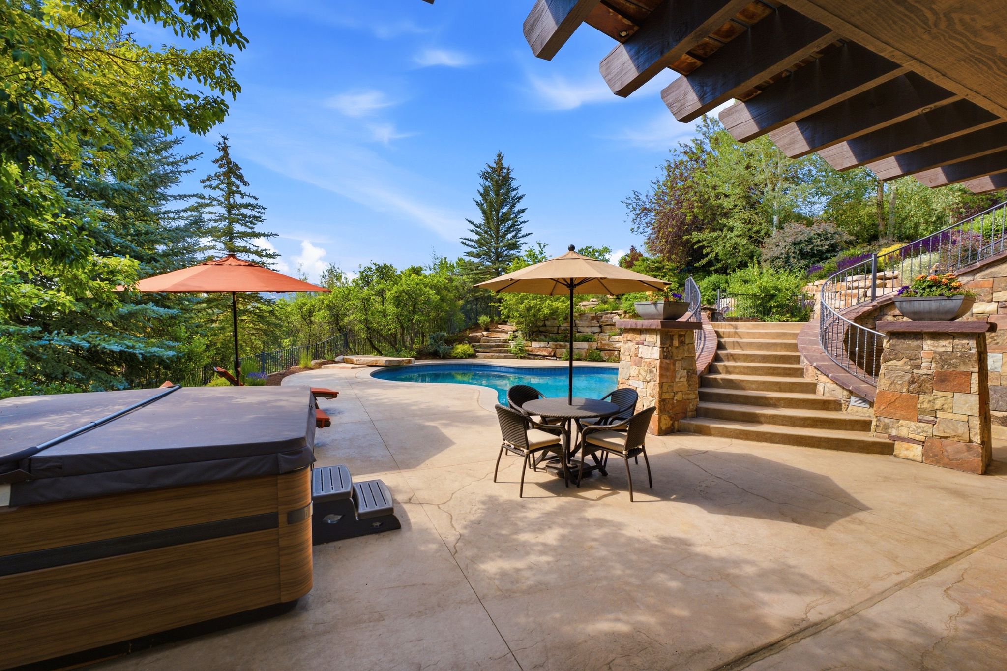 Outdoor living space featuring a built-in hot tub, concrete patio, inground swimming pool, stone retaining walls, and a curved stone staircase with a wrought iron railing