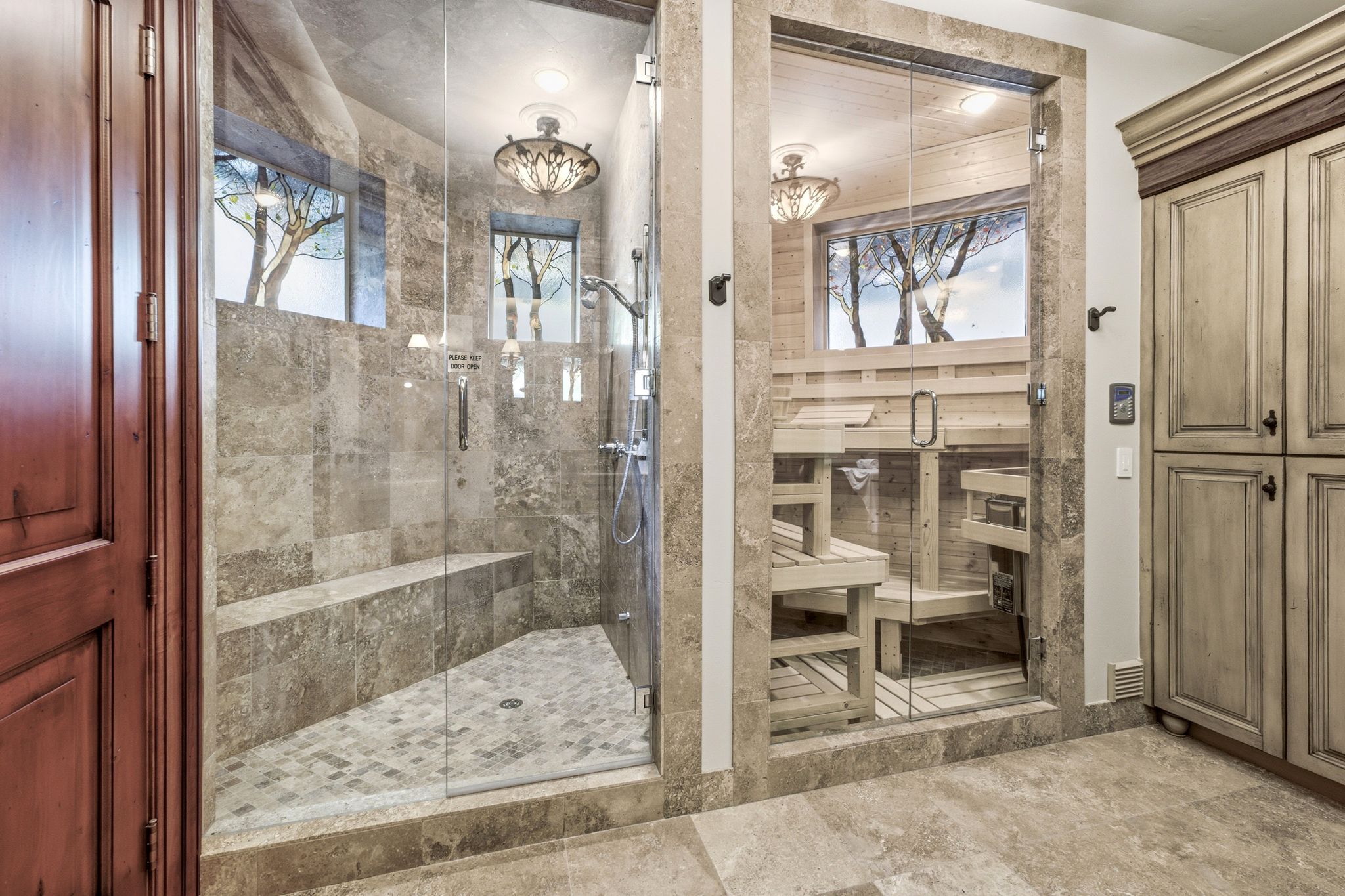 Spacious walk-in shower with a built-in bench and glass enclosure, complemented by a dedicated sauna featuring light wood benches