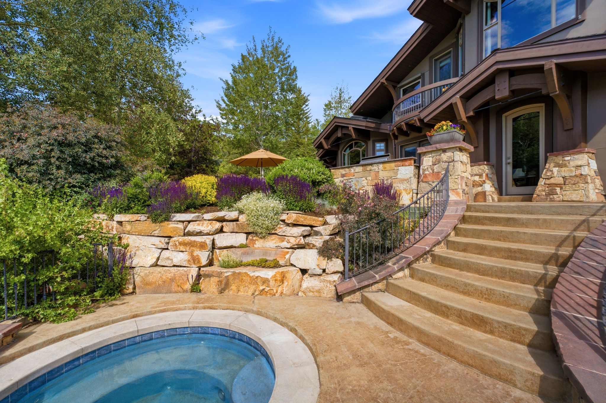 Outdoor spa with blue tile accents, surrounded by a stone retaining wall and mature landscaping