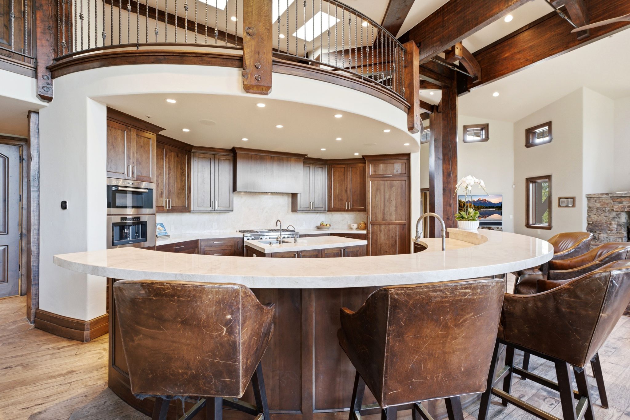 Gourmet kitchen featuring a curved island with stone countertop, wood cabinetry, stainless steel double oven, and wood-finish flooring