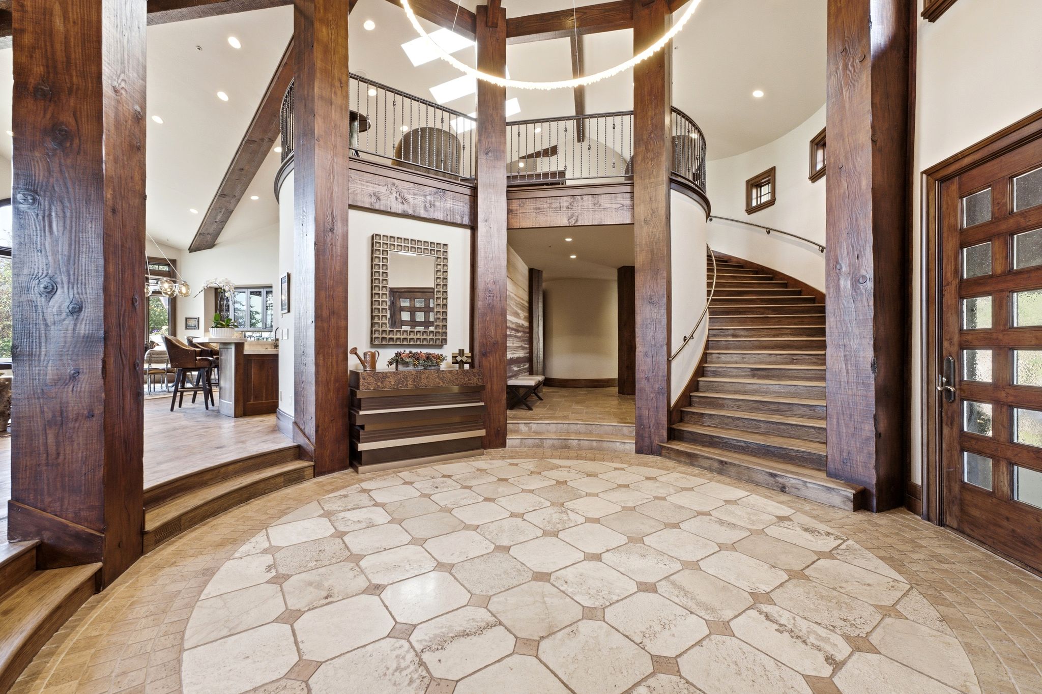 Grand foyer featuring a circular tiled floor inlay, exposed wood beams, a curving staircase with a wrought iron railing, a wood entry door with frosted glass panels, and recessed ceiling lighting