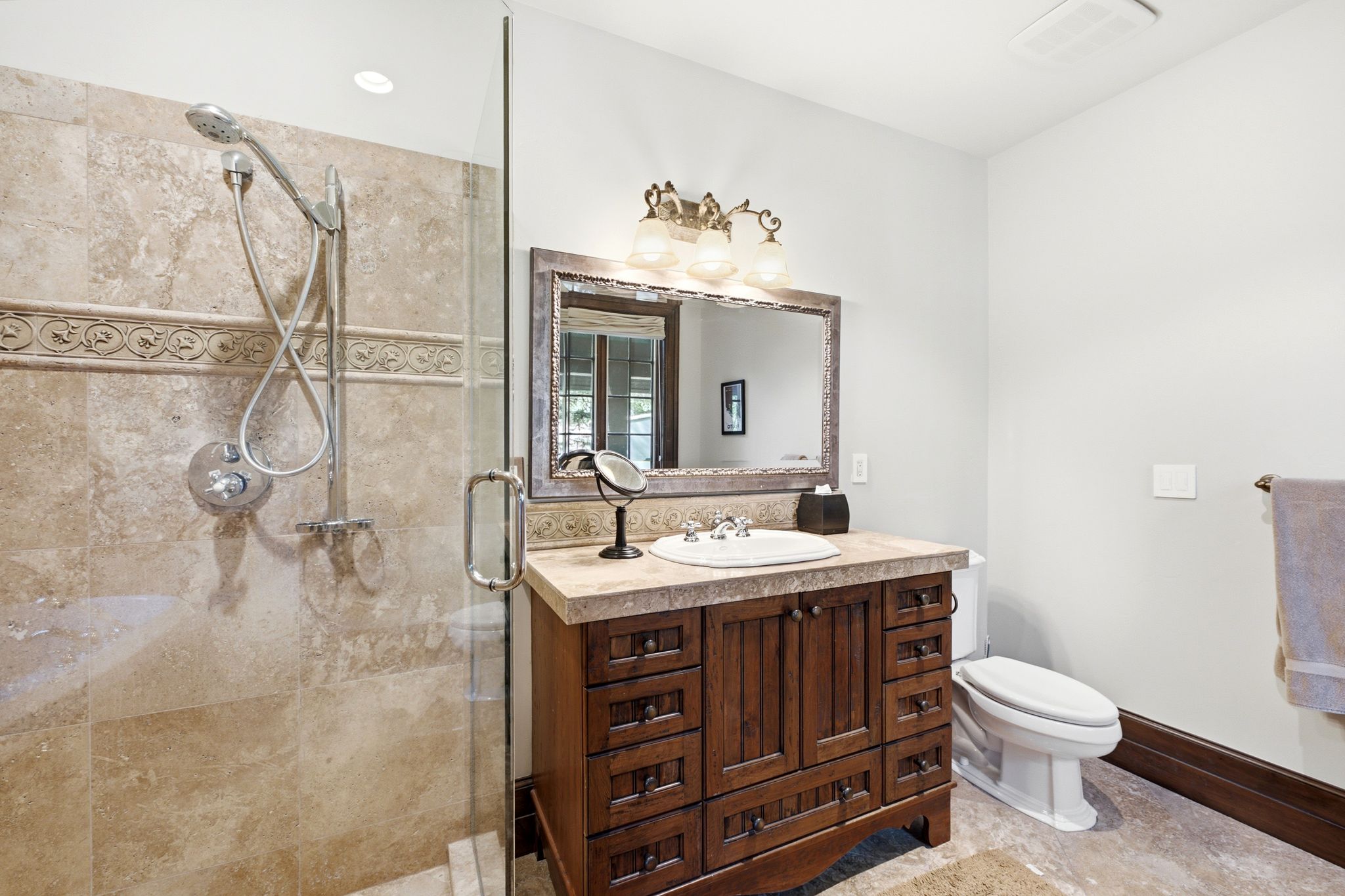 Glass-enclosed shower with stone tile surround and decorative accent band, featuring a handheld showerhead