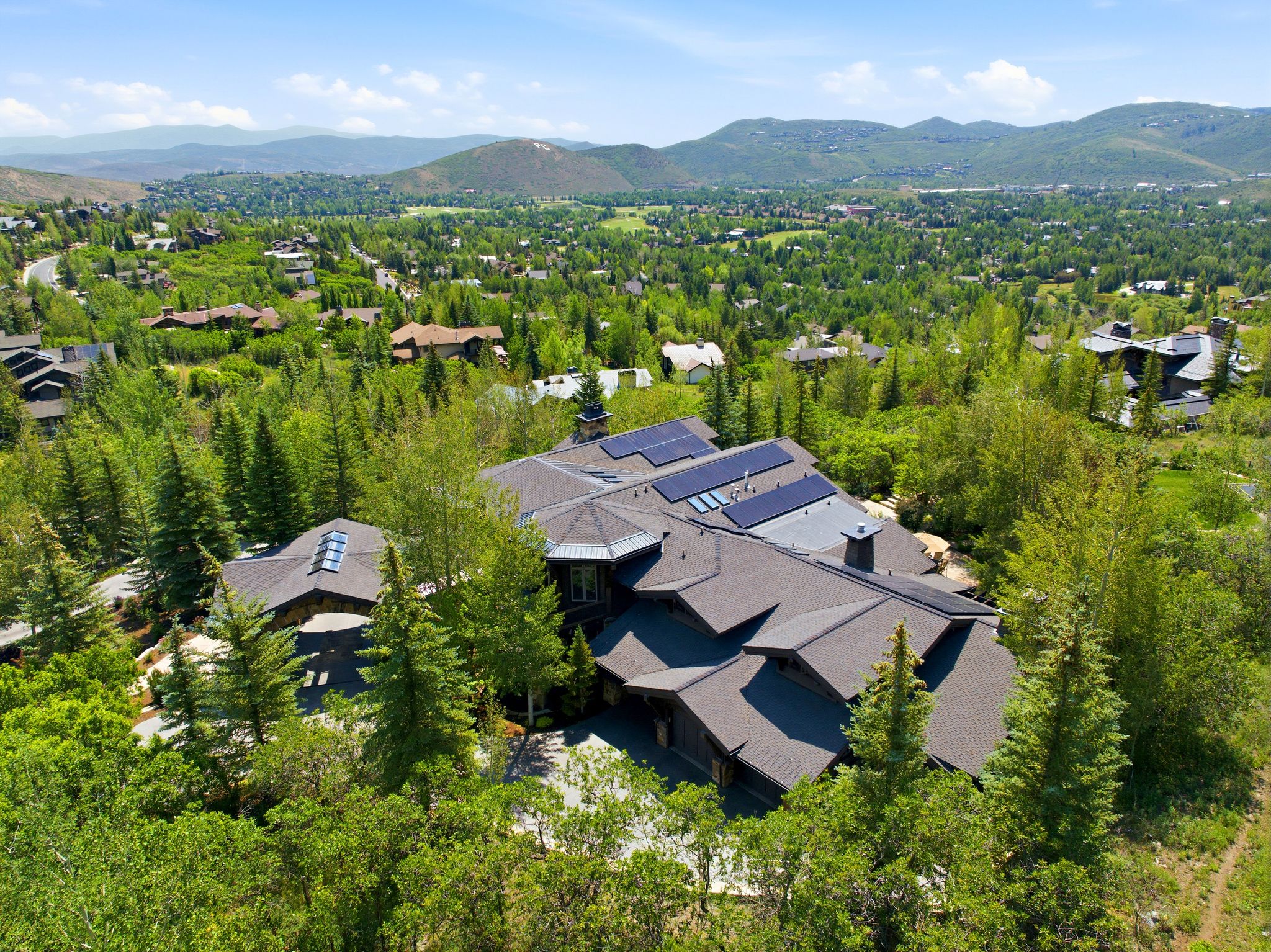 Expansive property with a multi-level roofline and numerous solar panels, surrounded by mature trees