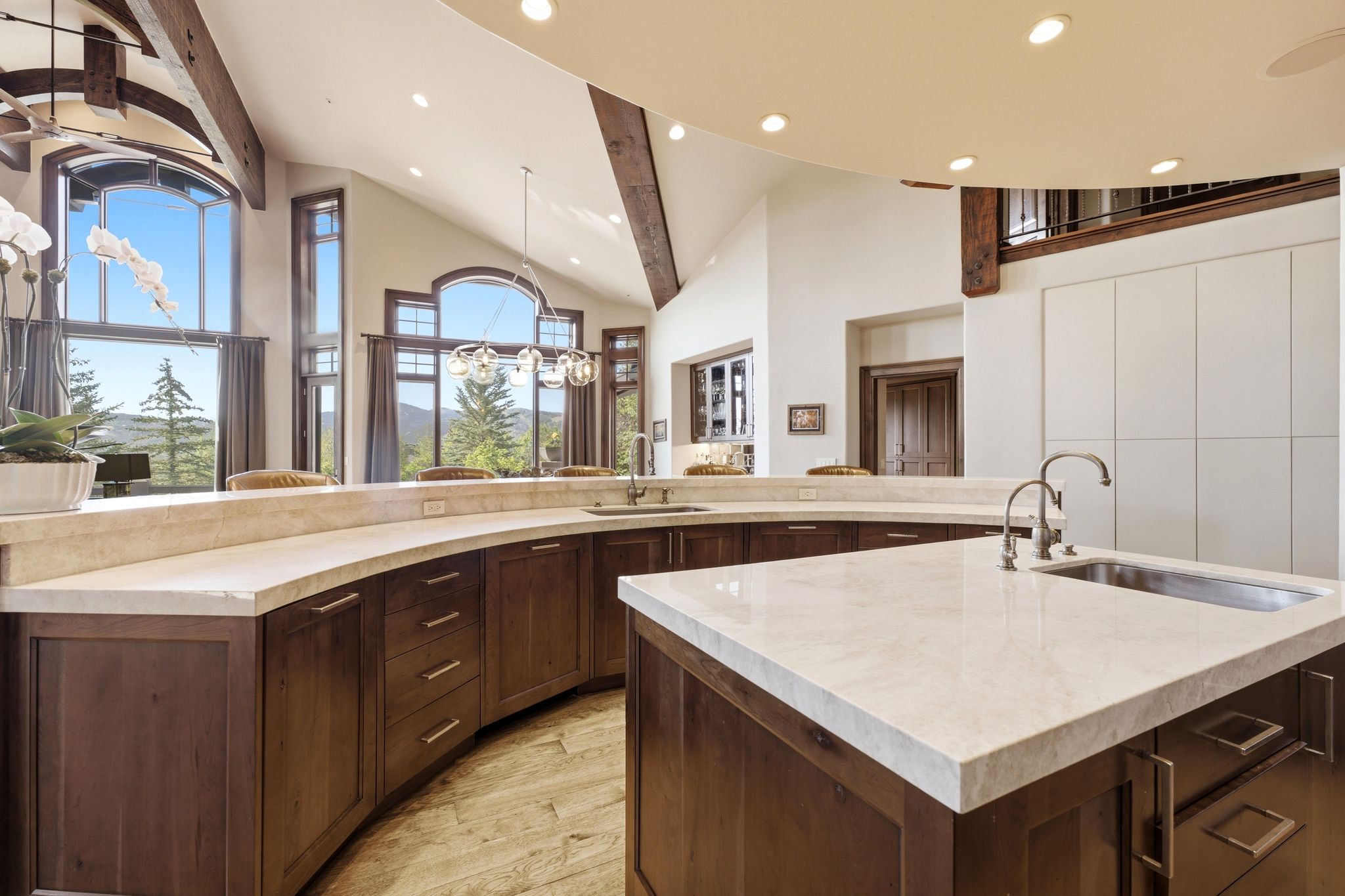 Kitchen featuring a center island with undermount sink, curved countertop bar seating, wood-finish cabinetry, and a vaulted ceiling with exposed beams