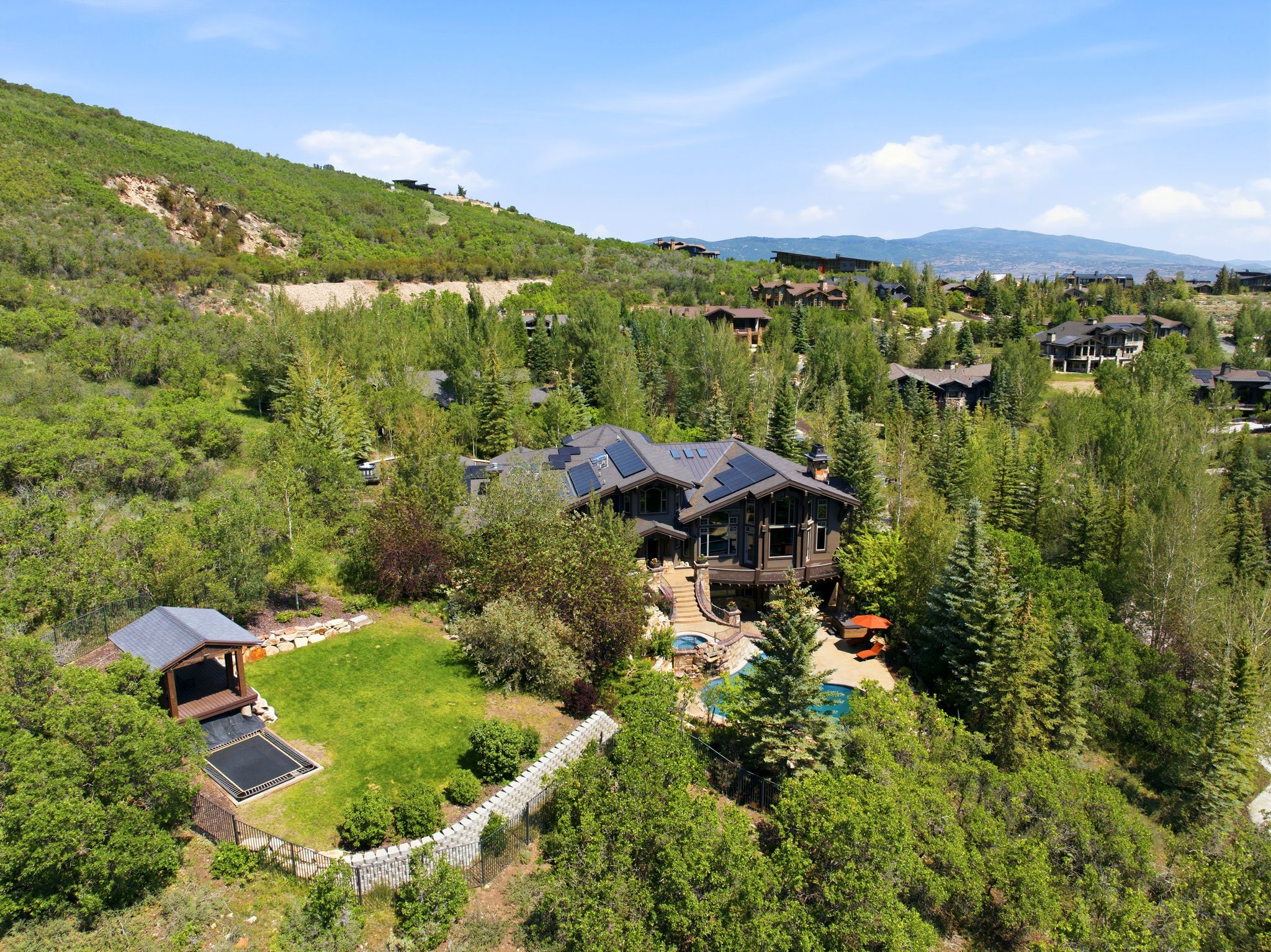 Elevated property featuring a multi-story residence with solar panels, a tiered outdoor entertaining area, and a swimming pool