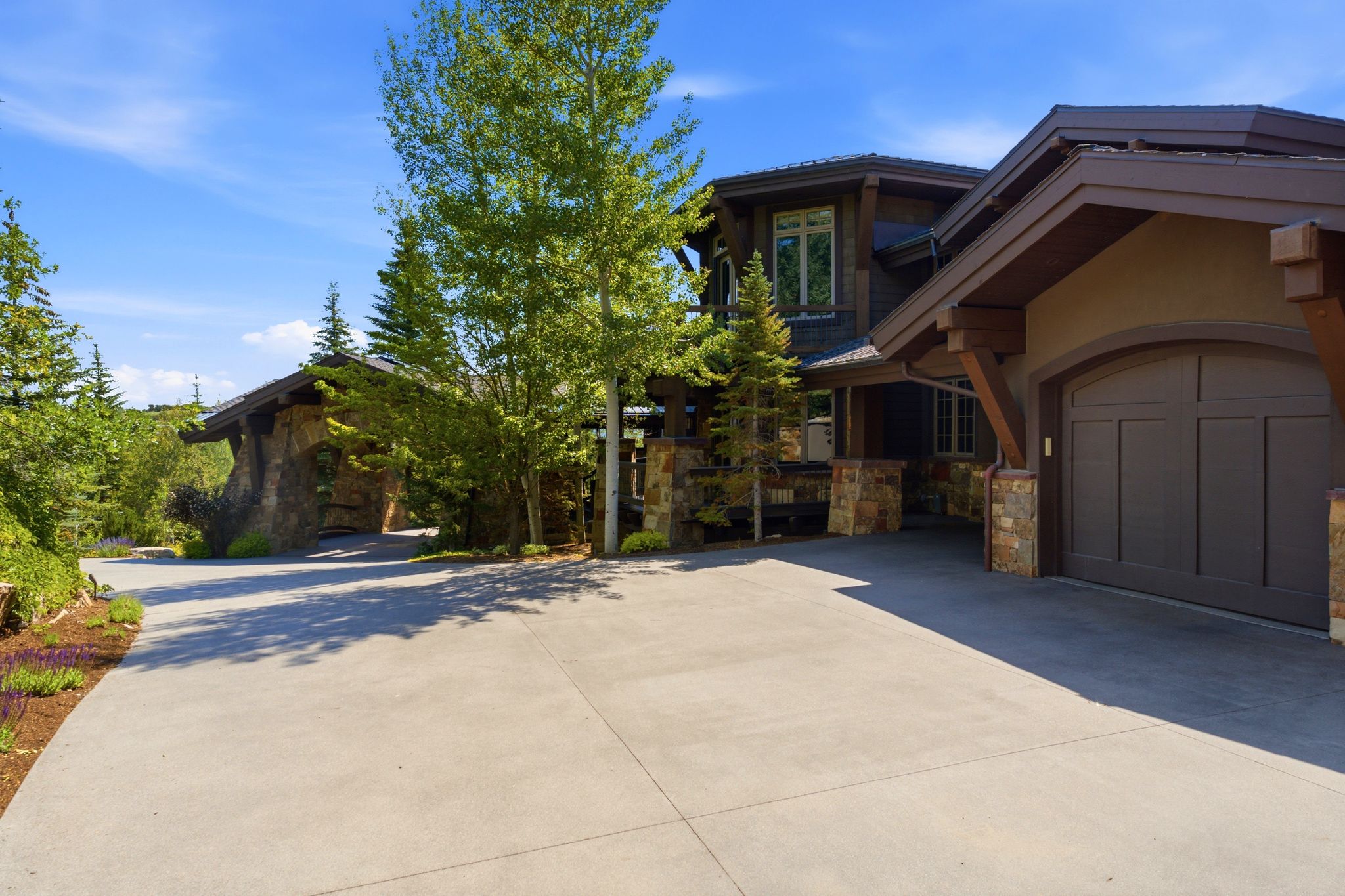 Exterior featuring a two-car garage with an arched door, stone facade accents, wood beam detailing, and a concrete driveway