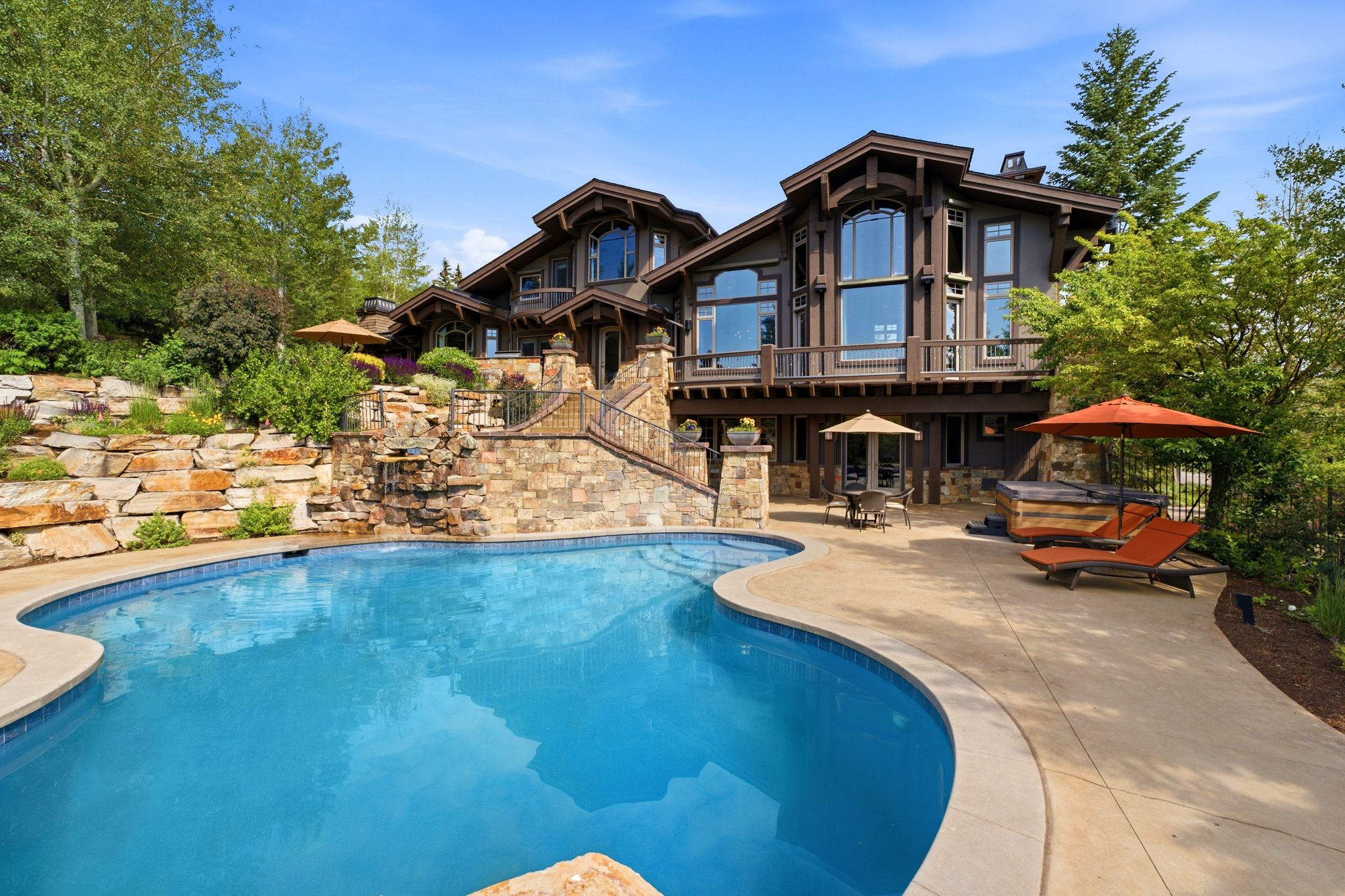 Expansive outdoor living area featuring a freeform swimming pool with integrated spa and waterfall, surrounded by concrete patio and stone retaining walls