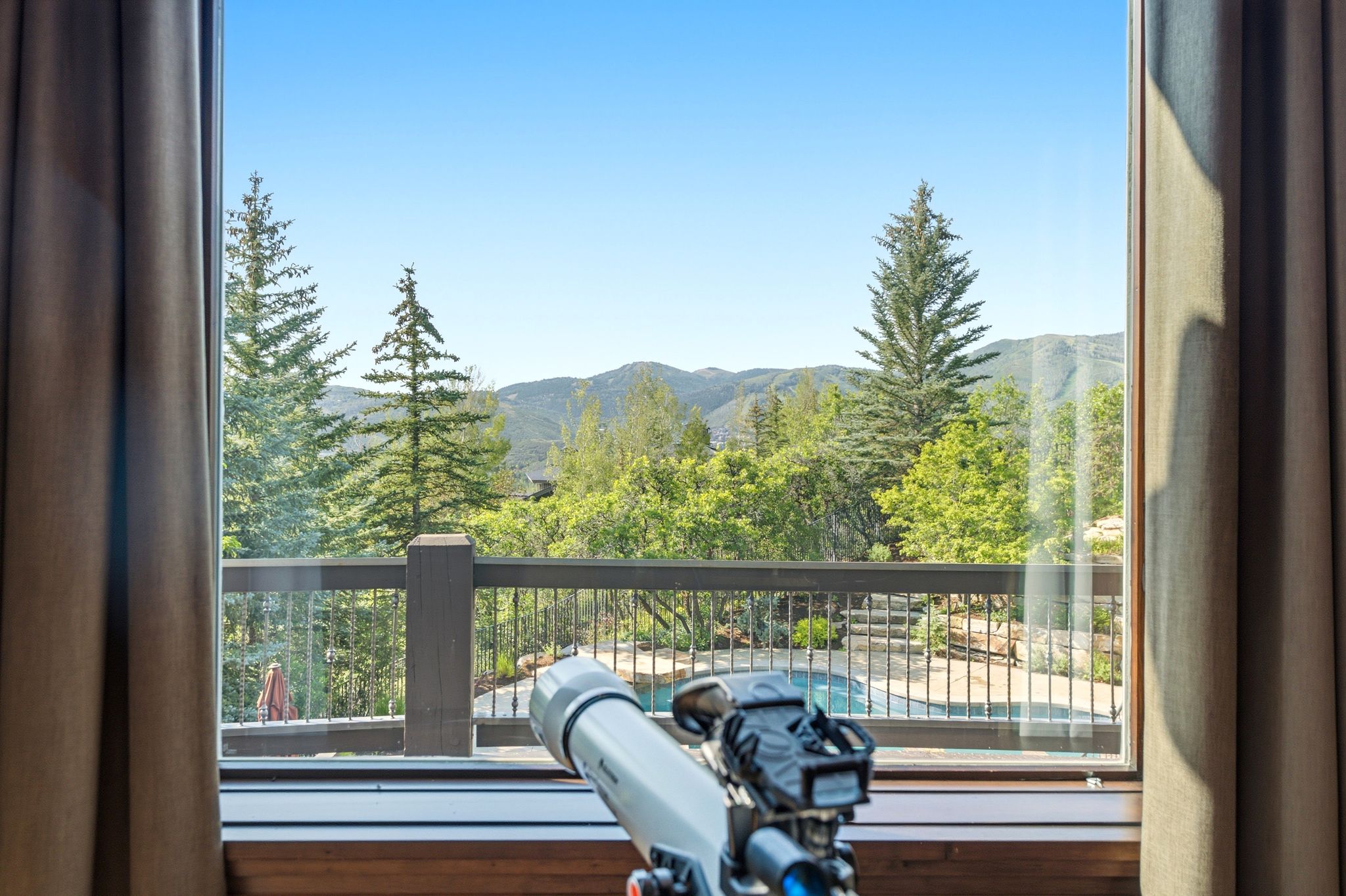 Expansive outdoor balcony with dark wood railings and metal spindles, offering broad mountain scenery
