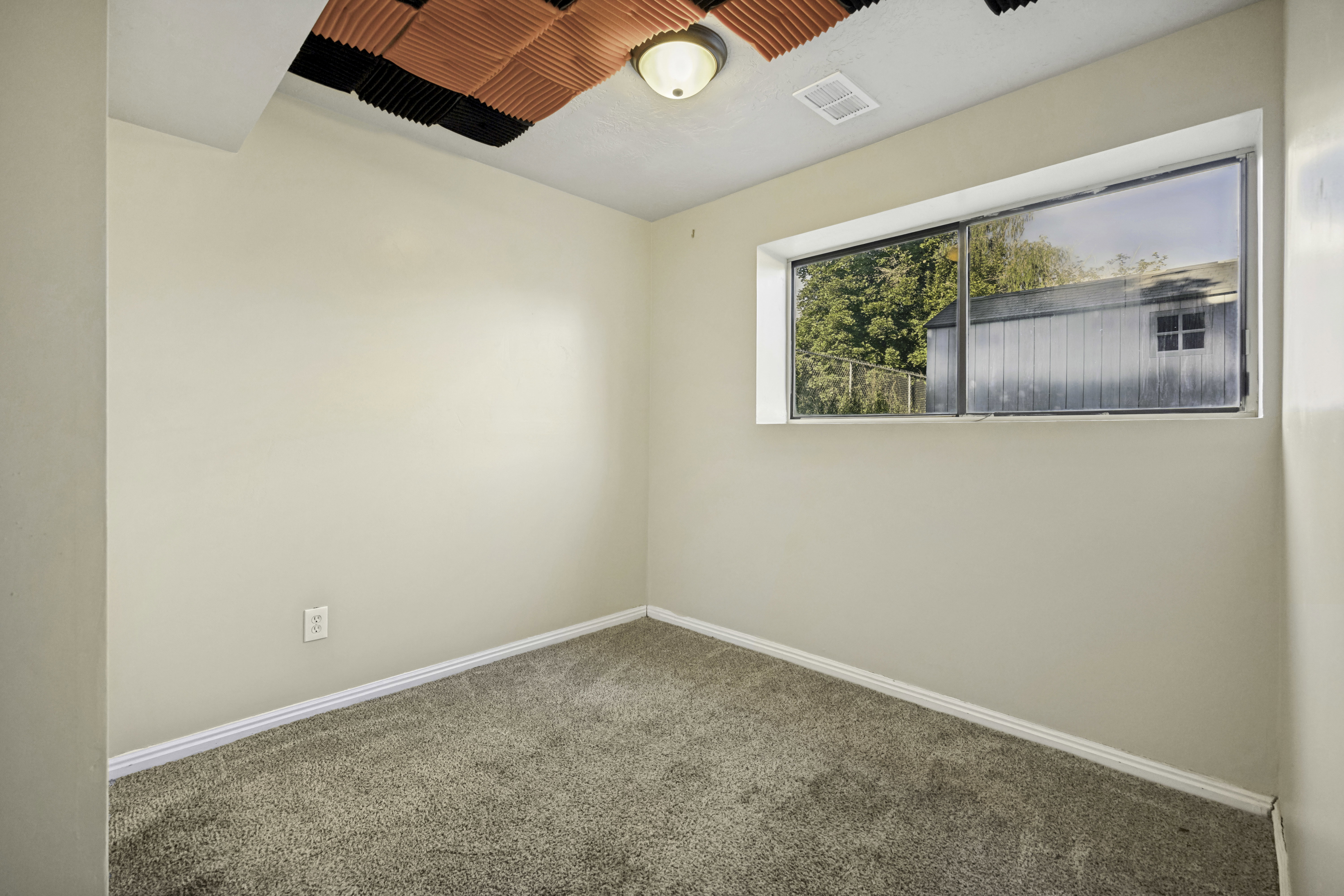 Carpeted room featuring a white baseboard, a single window, and a flush-mount ceiling light