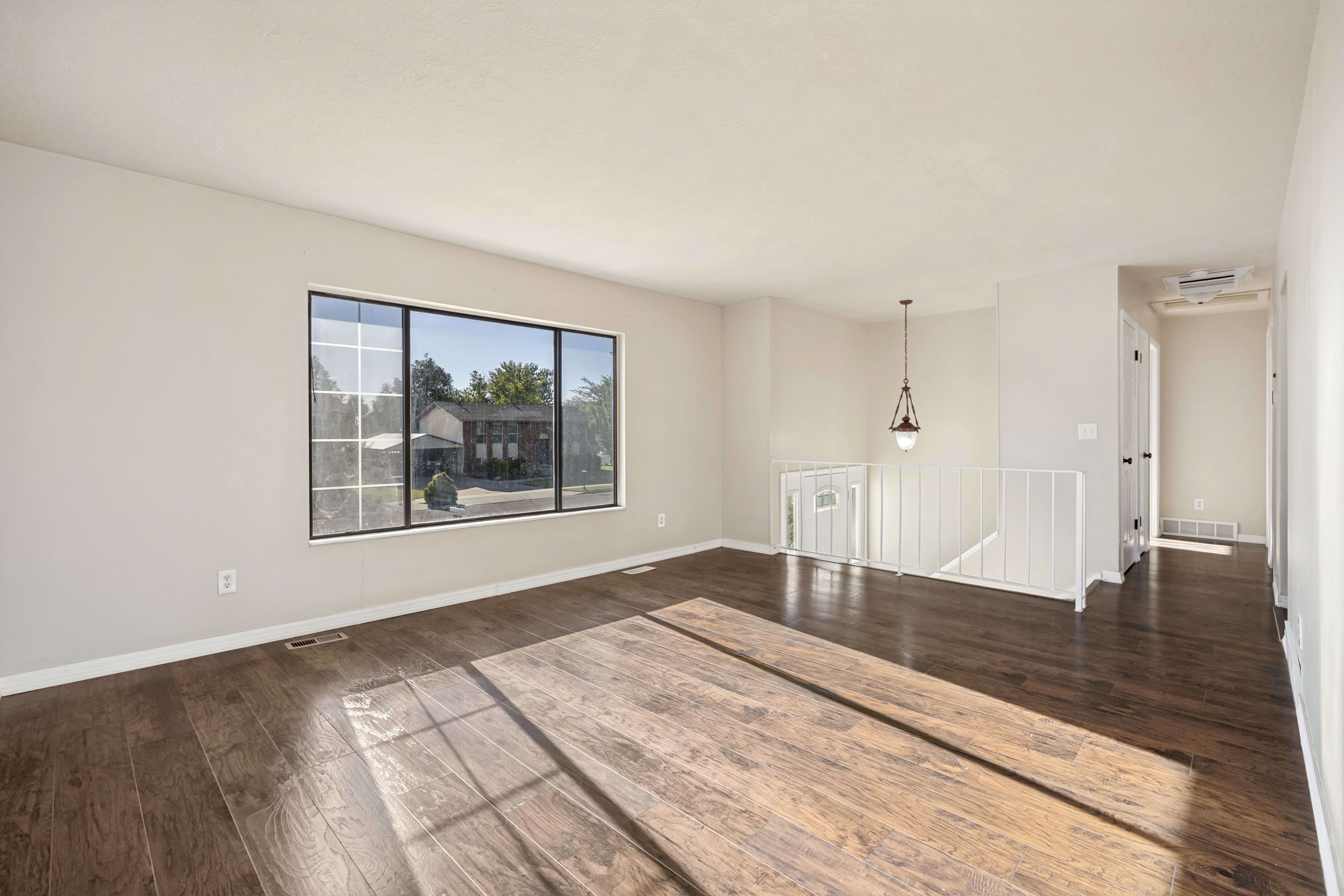 Spacious room featuring wood-finish flooring, a large multi-pane window with black trim, and light-toned wall paint