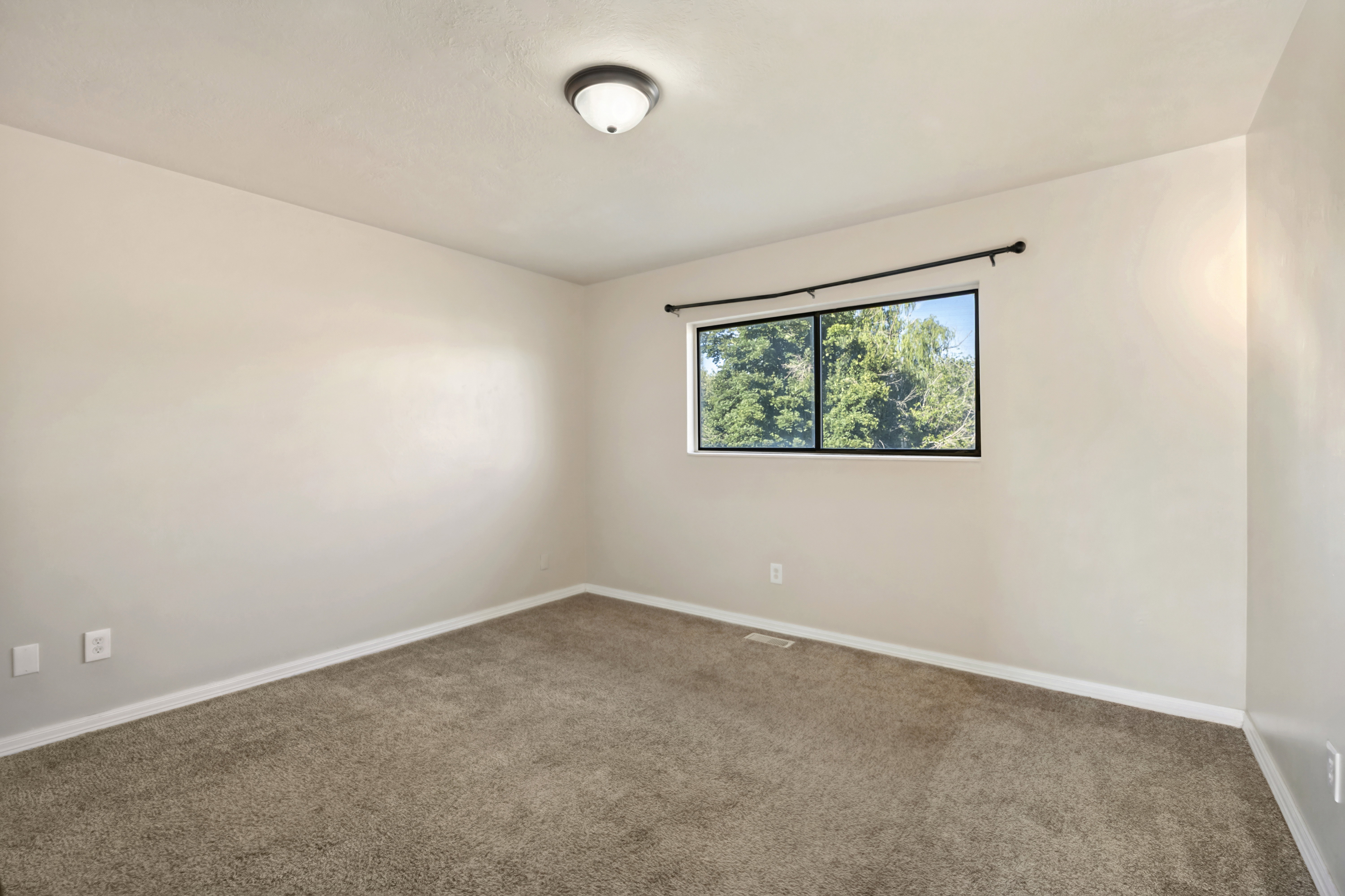Neutral-toned room featuring a large window with black trim, soft carpet flooring, and a flush-mount ceiling light fixture