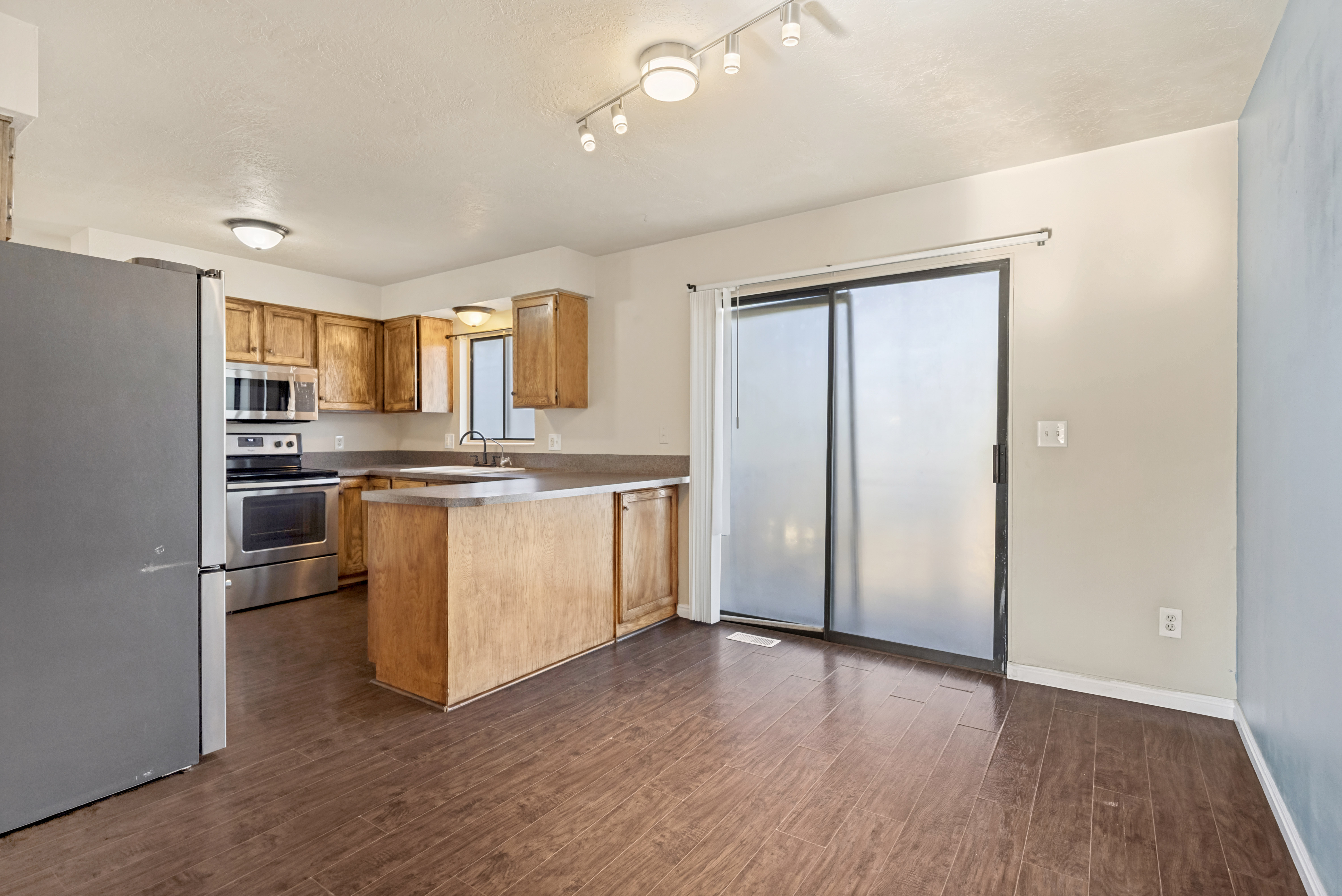 Kitchen featuring wood-finish flooring, light wood cabinetry, stainless steel appliances, and a sliding glass door