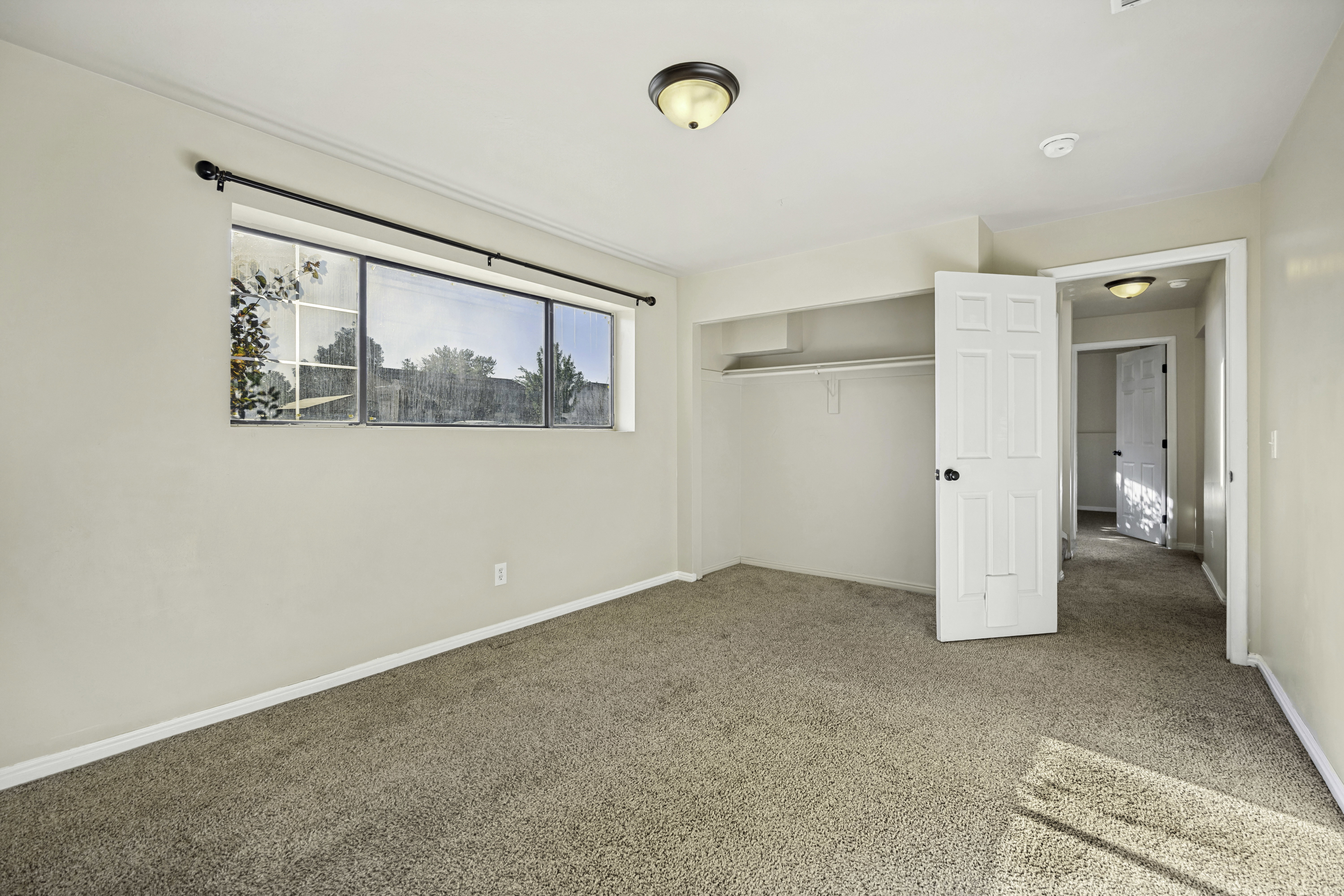 Carpeted interior space featuring a multi-pane window, flush-mount ceiling light, white paneled doors with black hardware, and an open closet with shelving and a clothes rod