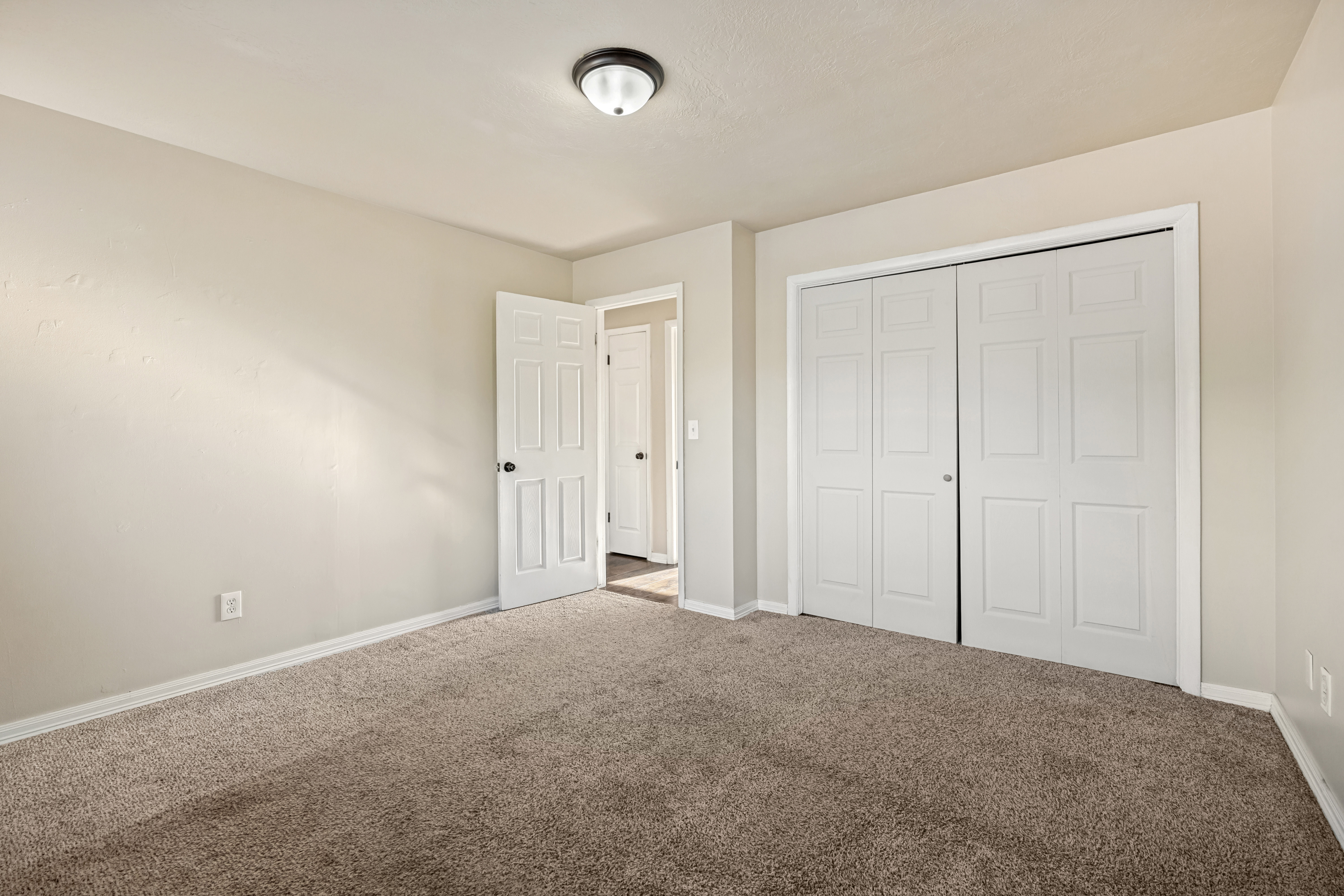 Carpeted room featuring a neutral wall palette, white trim, a semi-flush mount ceiling light, and bi-fold closet doors