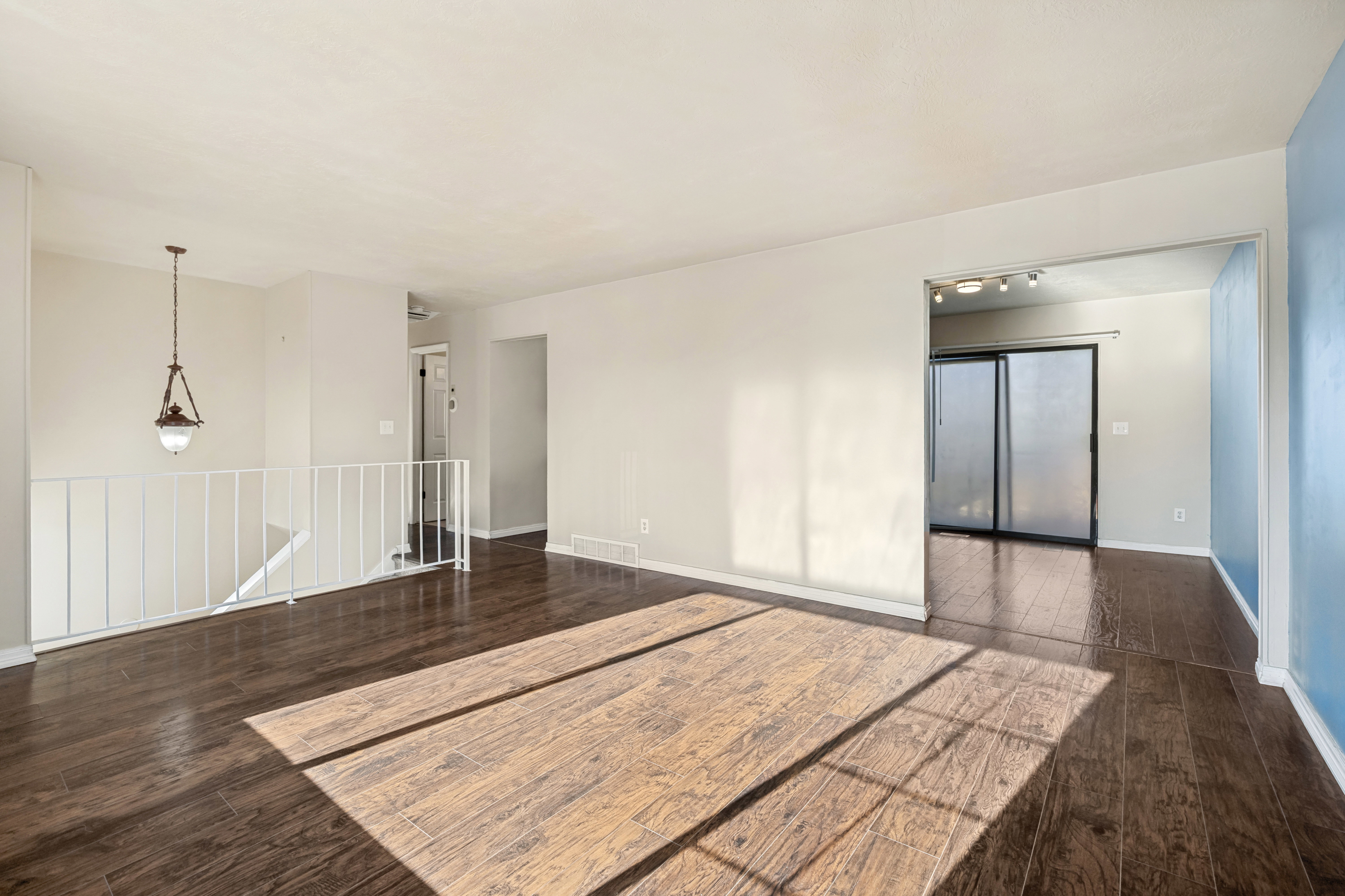 Spacious room featuring wood-finish flooring, a contemporary hanging light fixture, and a white railing