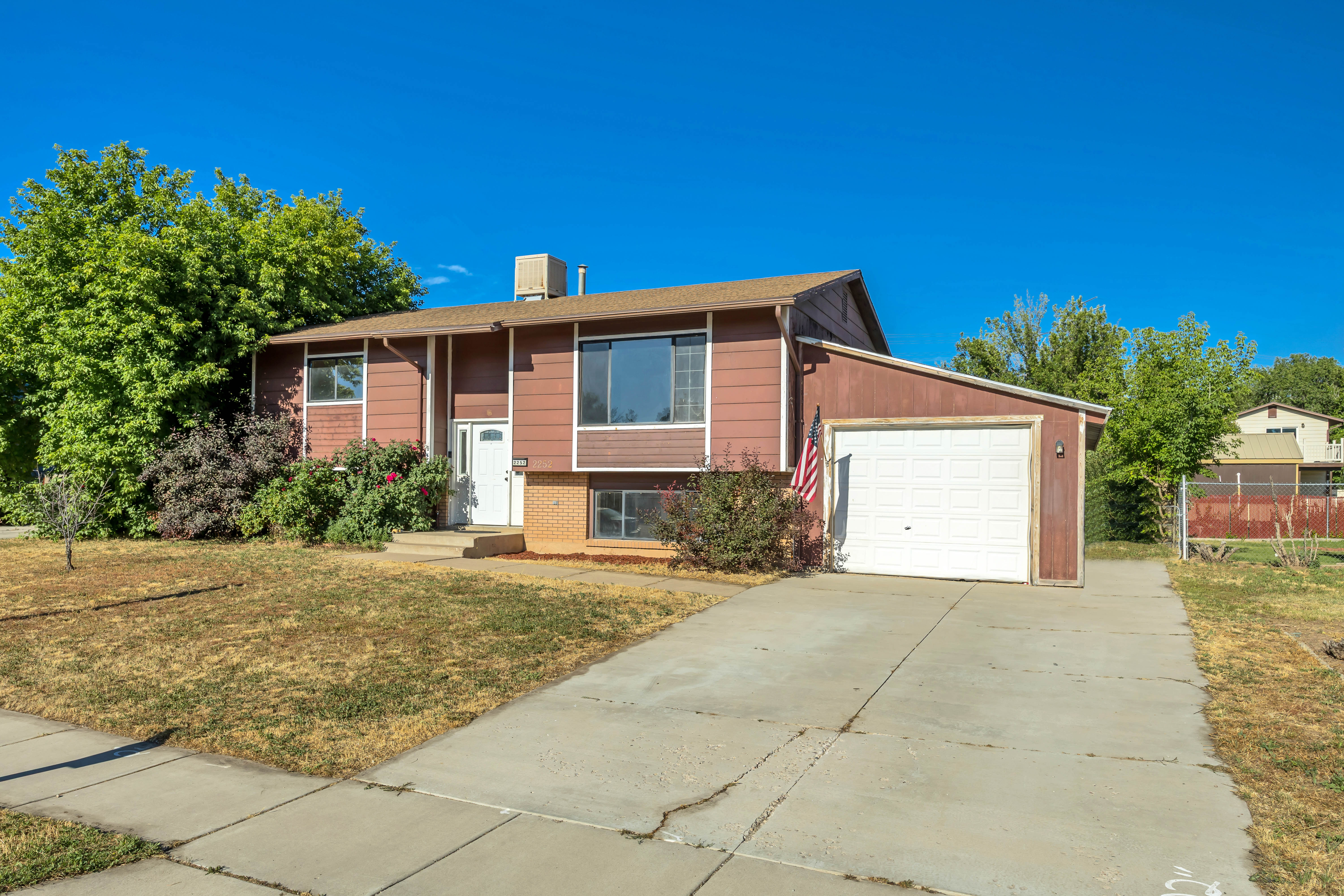 Split-level residence featuring a brown exterior with white trim, an attached single-car garage, a concrete driveway, and a white entry door