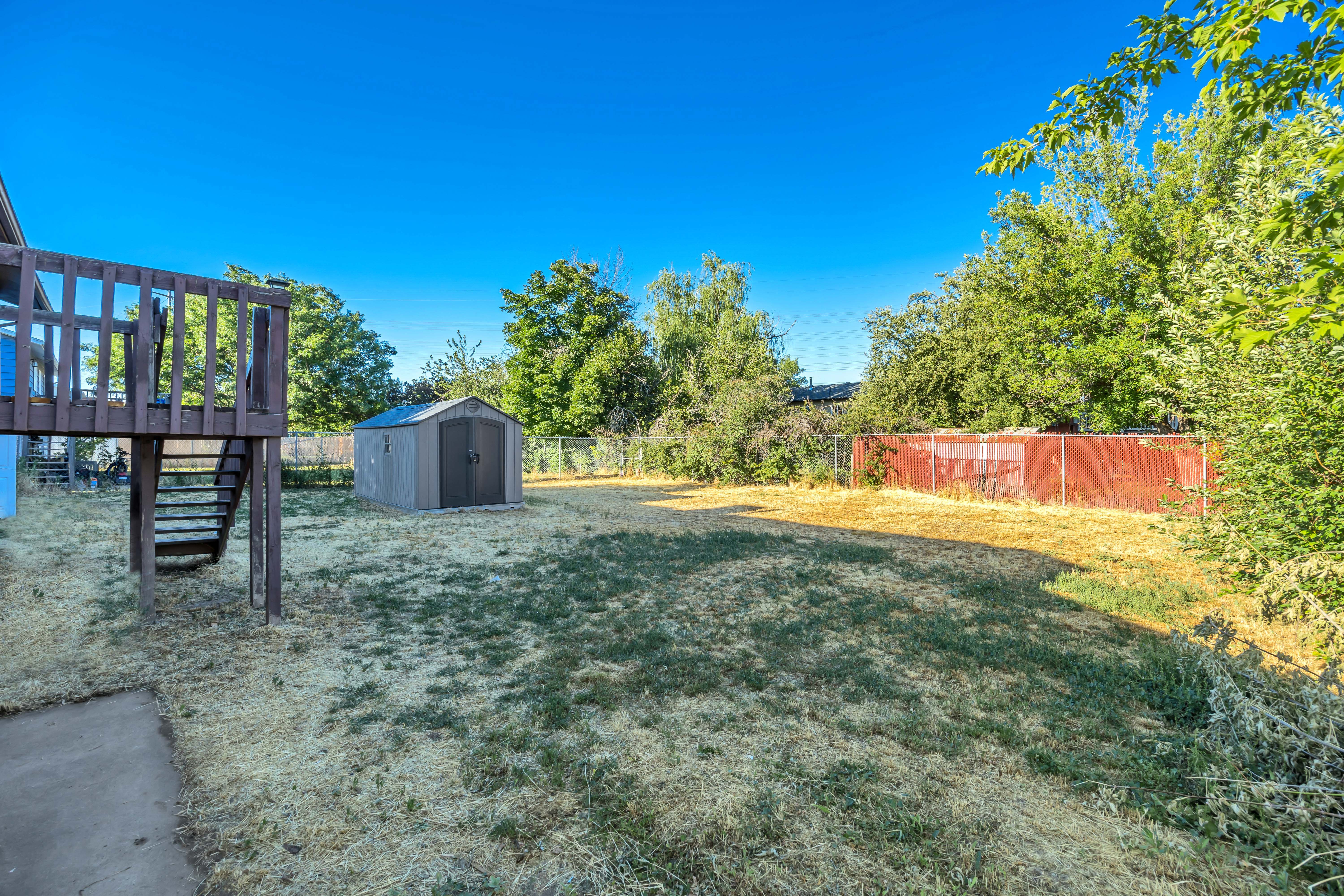 Expansive backyard featuring a wood-tone deck with stairs, a detached storage shttps://www.utahrealestate.com/lip/photo/listno/2169270#hed does not convey with purchase, chain-link fencing, and mature perimeter trees
