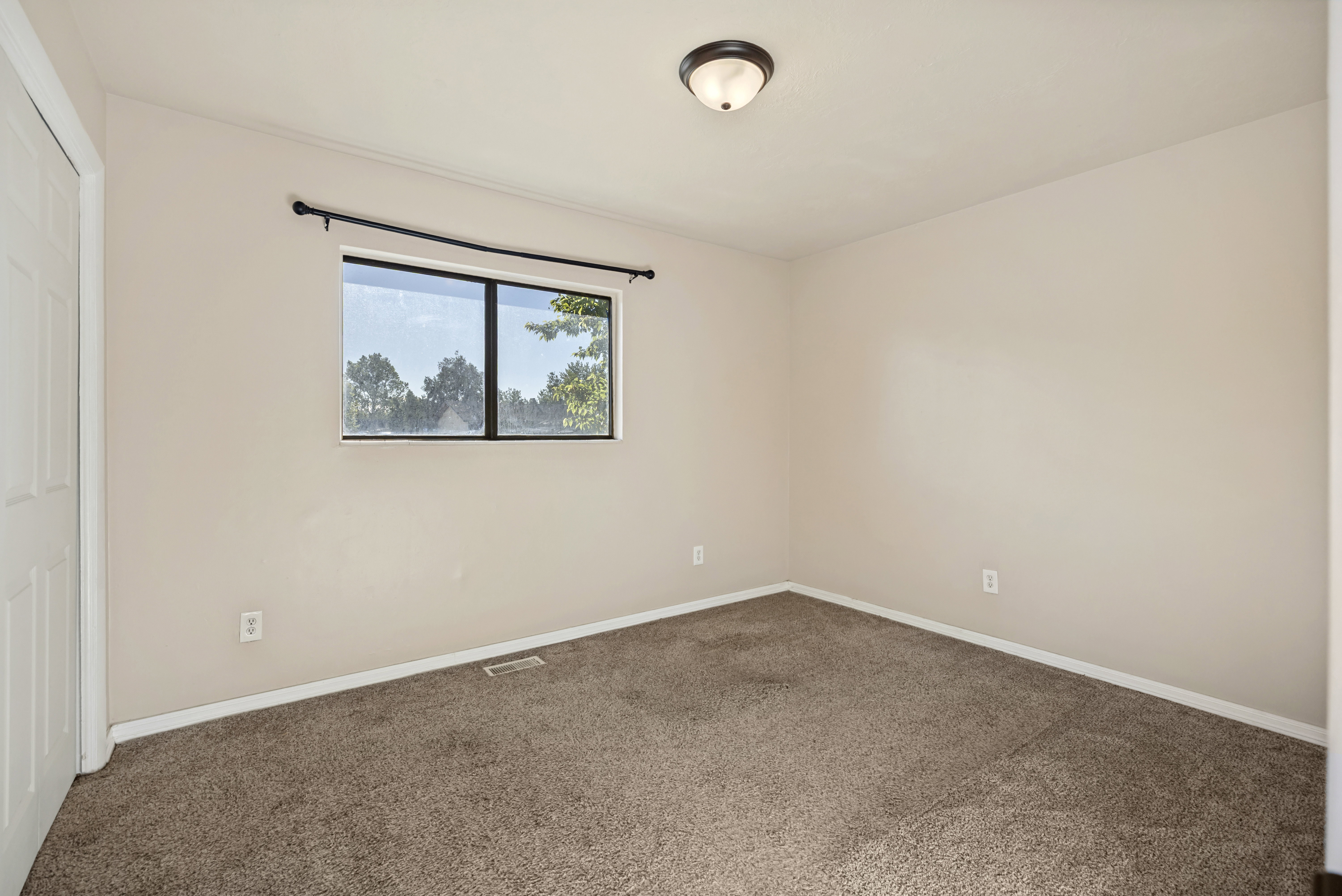 Spacious room featuring neutral painted walls, brown carpet flooring, a single window with a dark frame, a white bi-fold door, and a ceiling-mounted light fixture