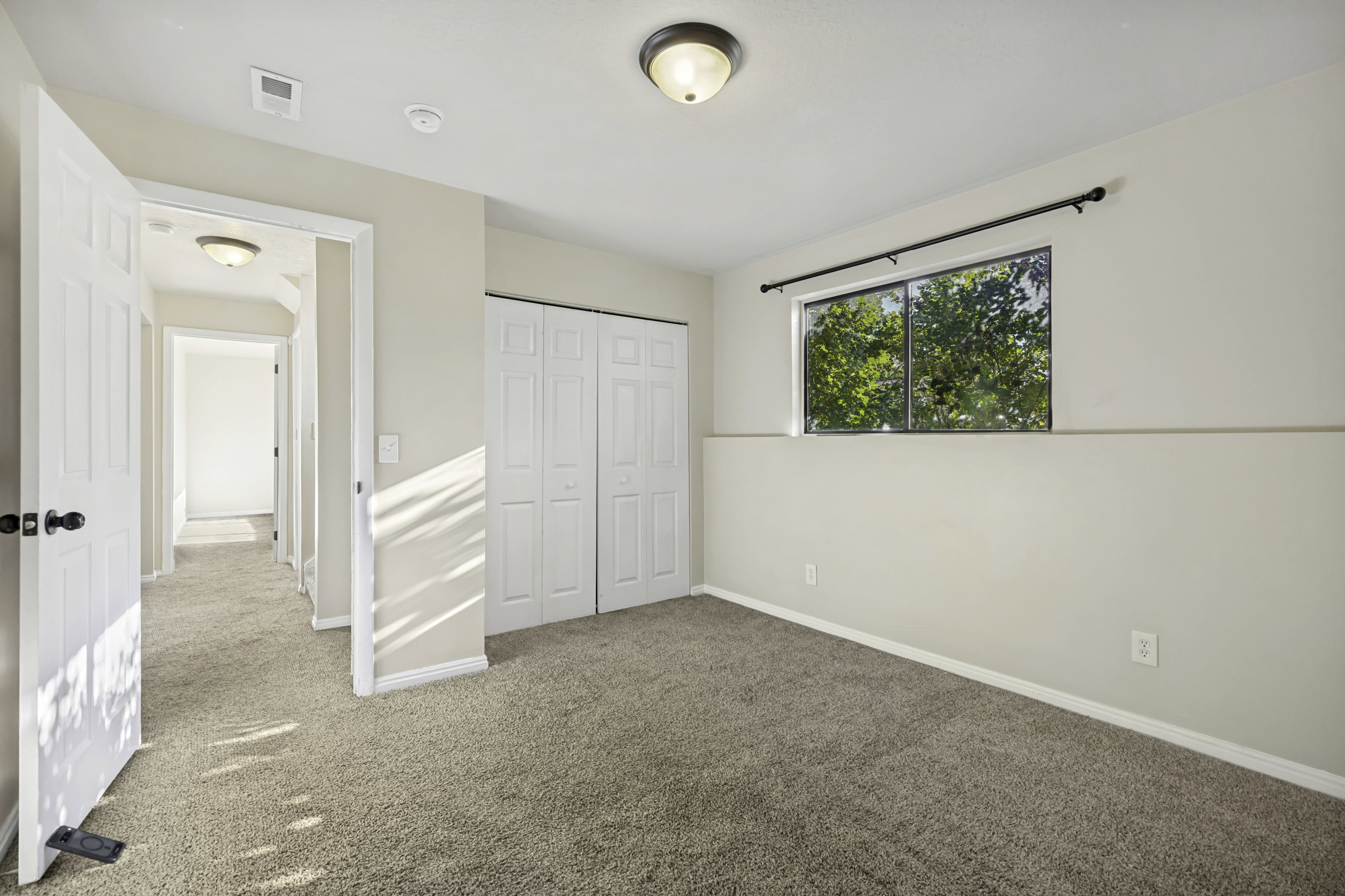 Carpeted room featuring a double bi-fold closet, a window with a dark curtain rod, and a flush-mount ceiling light