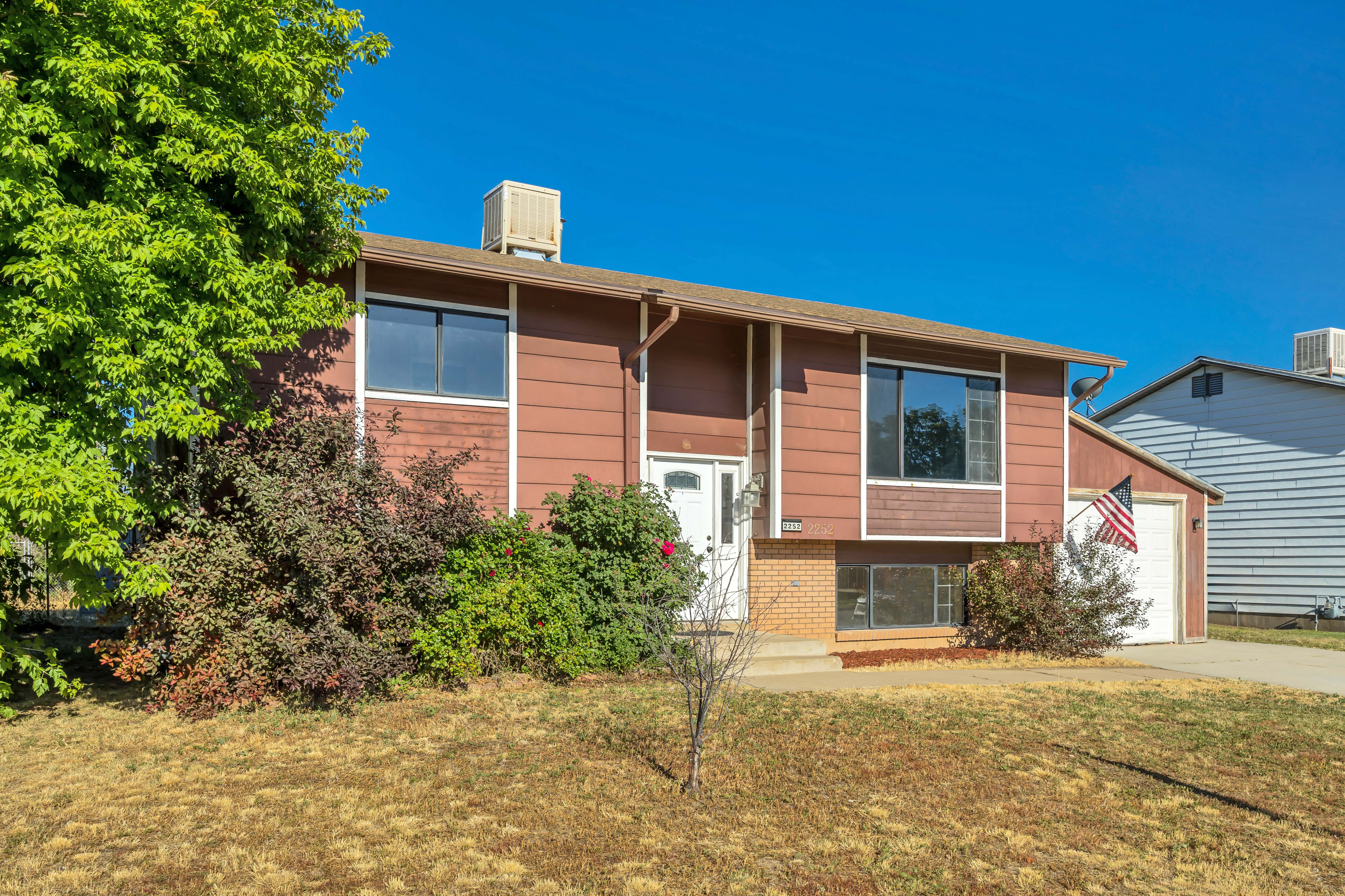 Split-level residence featuring a brown siding exterior, attached garage, white entry door, and mature landscaping