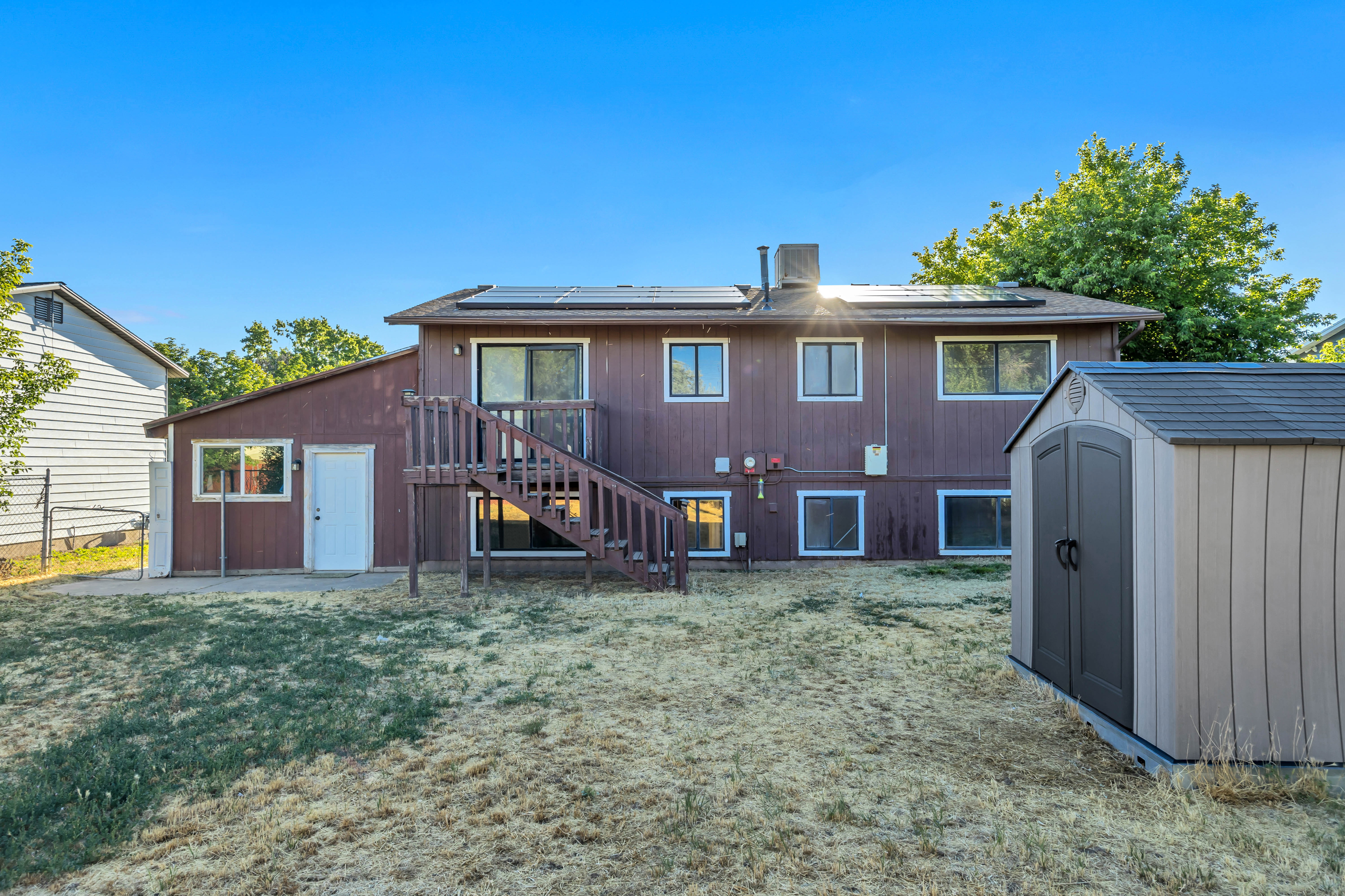 Back exterior with dark brown siding and a multi-level deck featuring a staircase. Shed storage does not convey