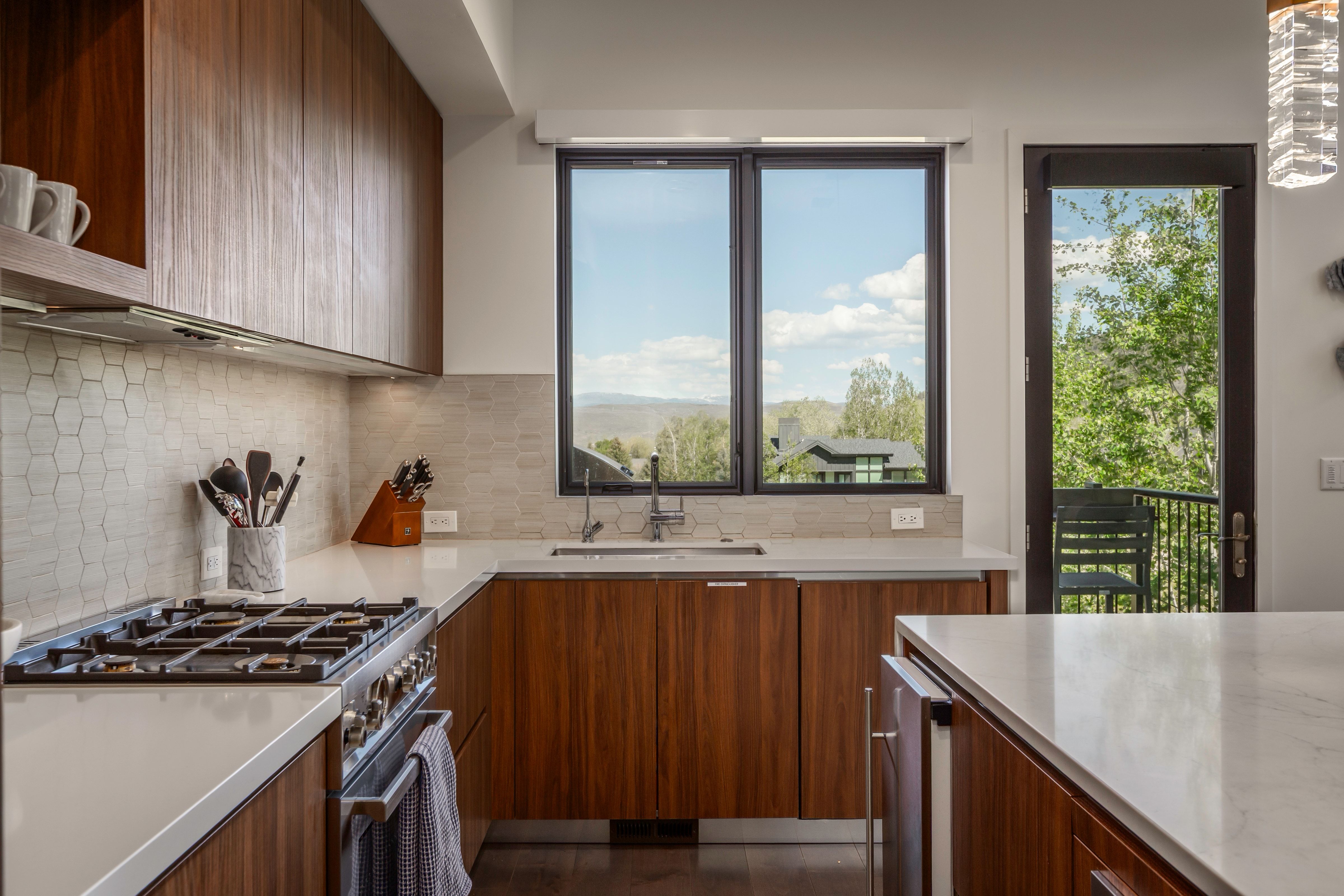 Gourmet kitchen featuring a gas range, wood-finish cabinetry, light stone countertops, and a full-height tile backsplash