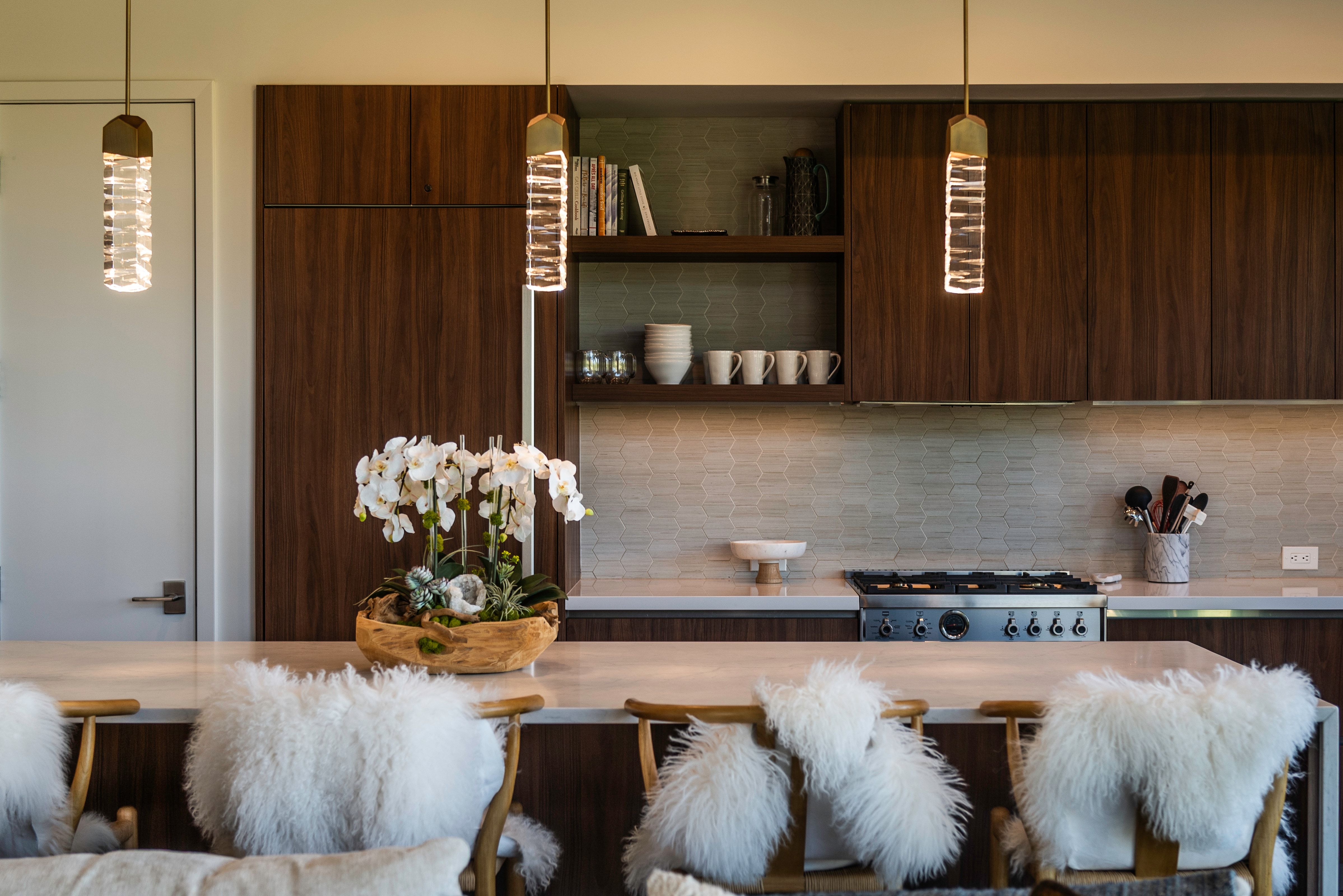 Kitchen island with a light-toned countertop, wood-finish cabinetry, stainless steel range, geometric tile backsplash, and two contemporary pendant lights