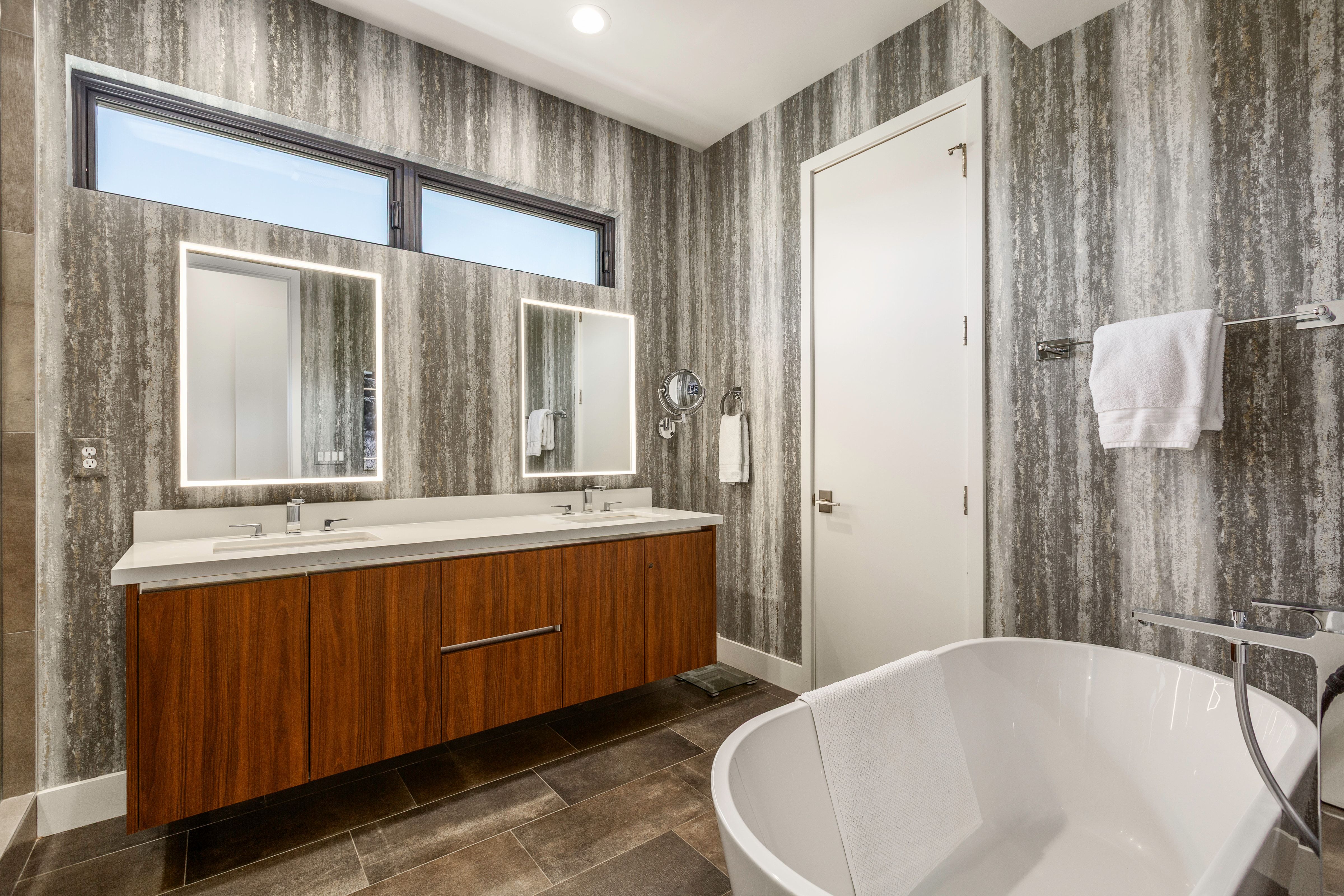 Bathroom featuring a freestanding soaking tub, a floating wood-finish double vanity with dual undermount sinks, and illuminated rectangular mirrors
