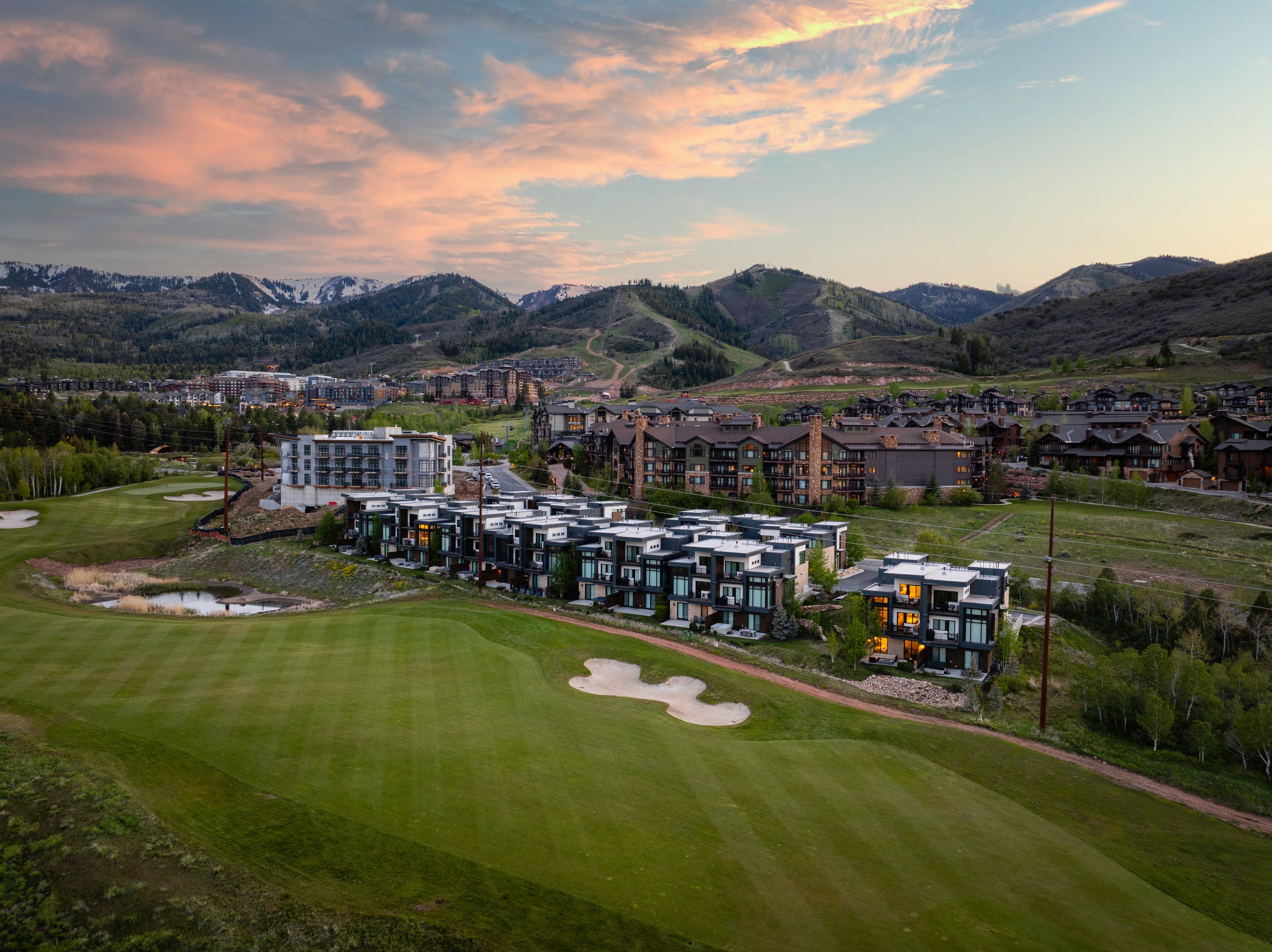 Expansive golf course frontage with a sand trap and water feature, complemented by modern residential buildings featuring dark siding and light trim