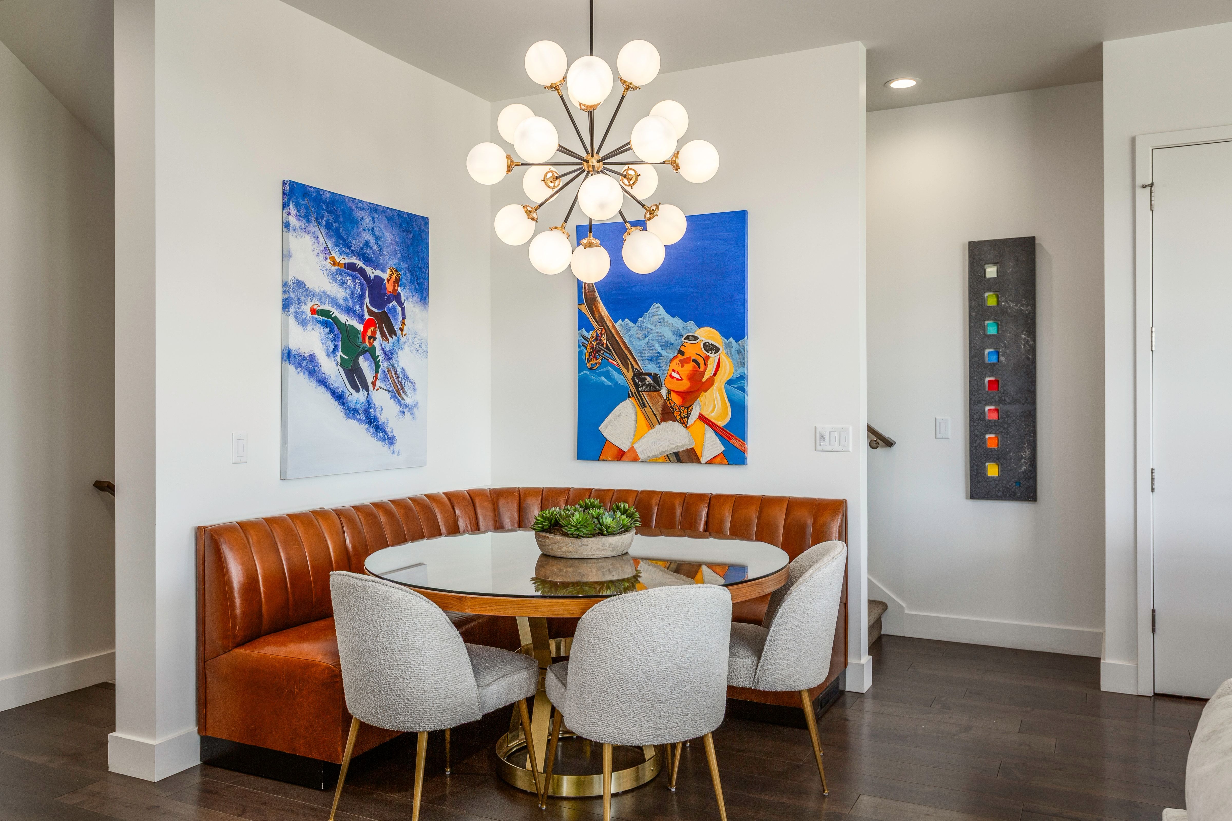 Dining area featuring a built-in tan upholstered banquette, a round glass-top table with a gold-tone base, and dark wood-finish flooring