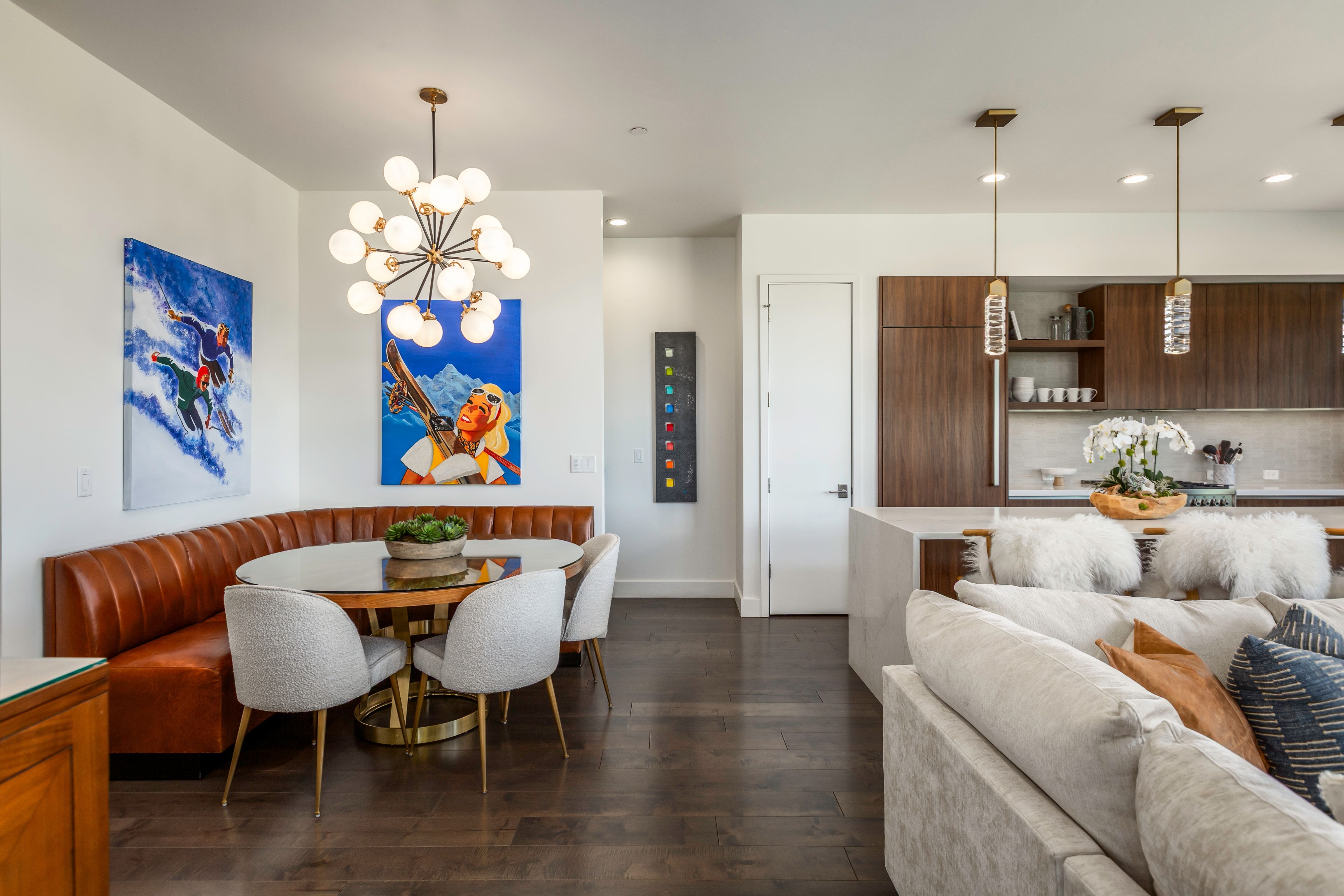 Open-concept living space featuring wood-finish flooring, a contemporary dining area with built-in seating, and a modern kitchen with integrated appliances and pendant lighting