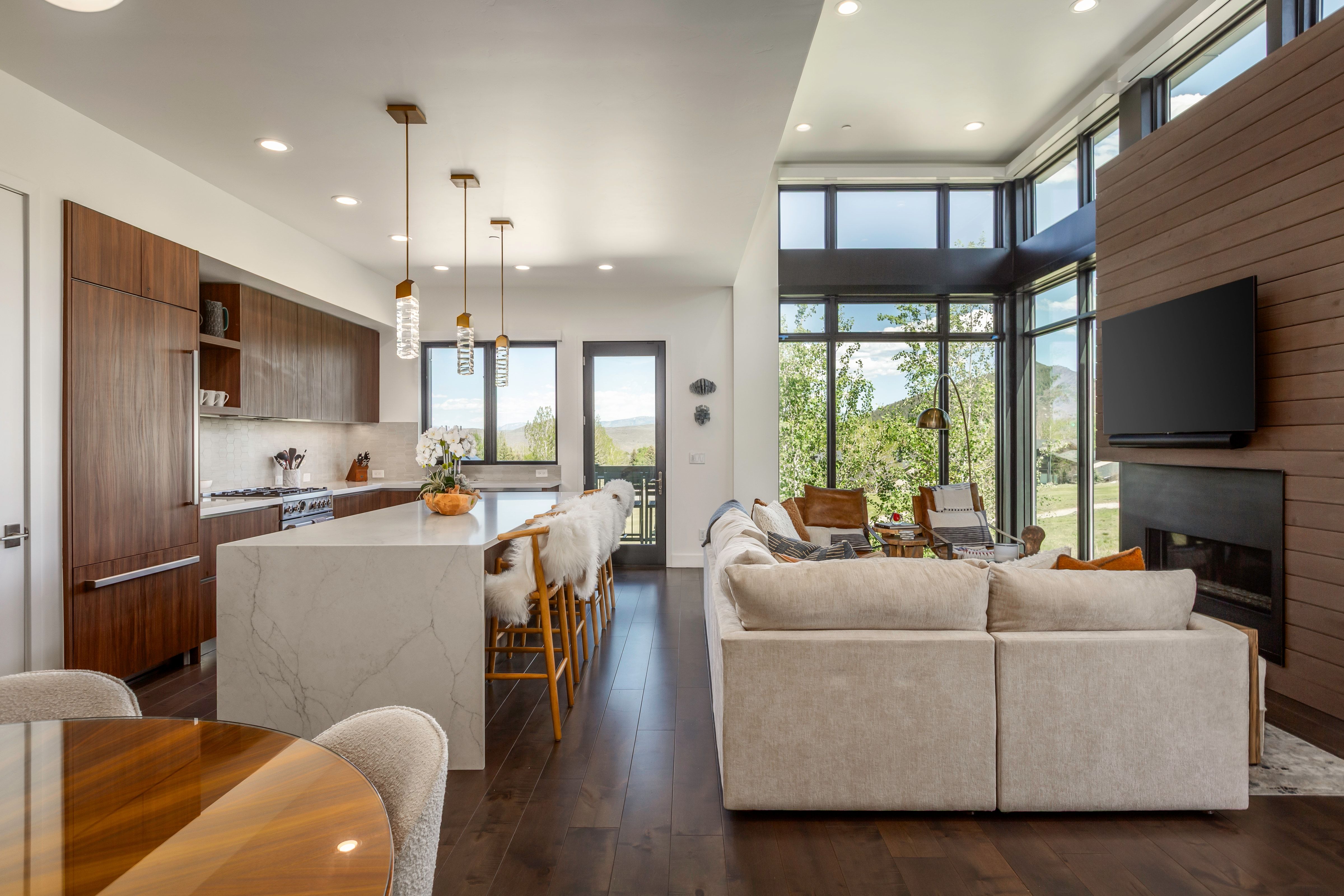 Open-concept living space featuring a gourmet kitchen, floor-to-ceiling windows, a built-in fireplace, rich wood-finish flooring, and recessed lighting throughout