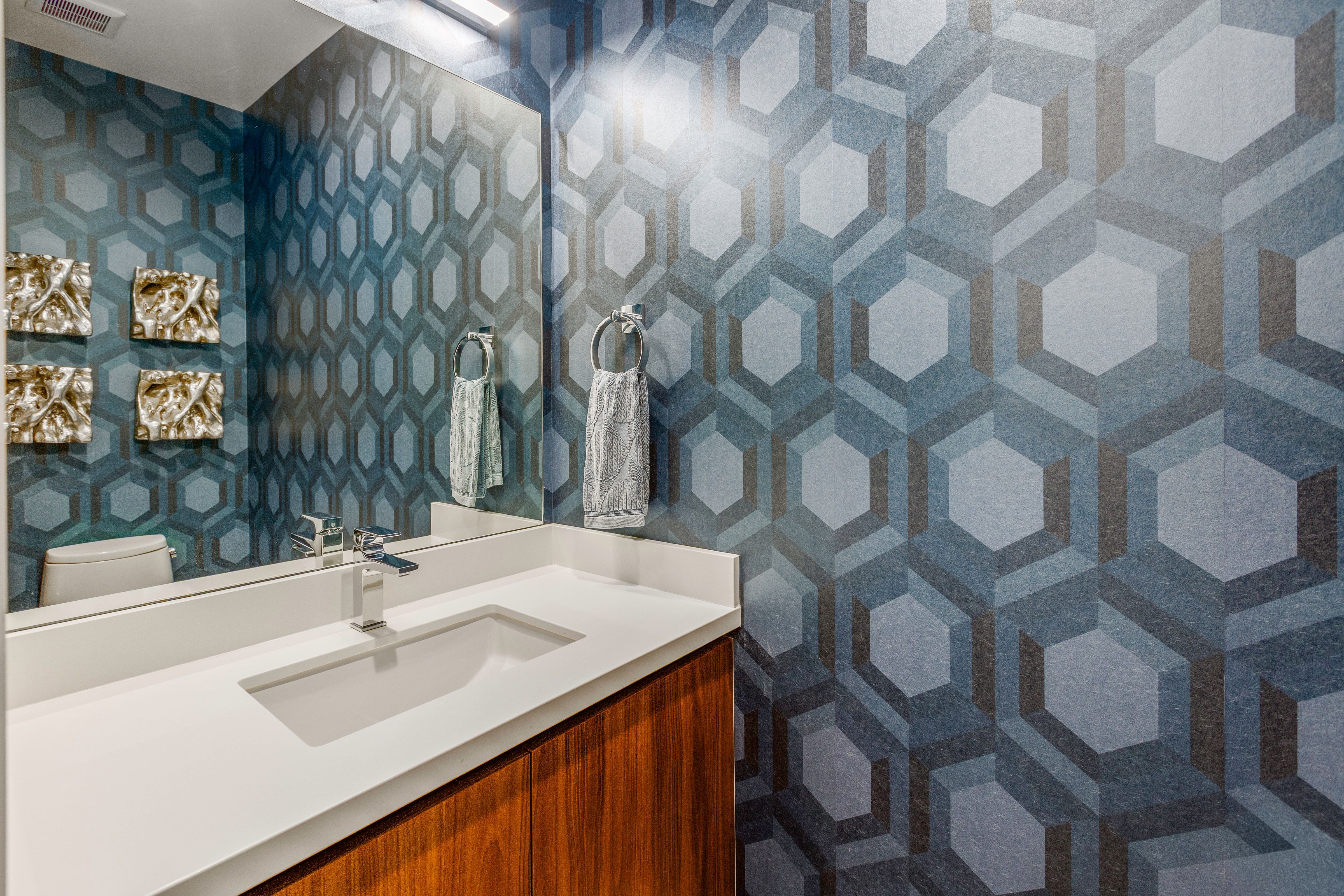 Bathroom featuring geometric patterned wallpaper, a wall-mounted mirror, a modern vanity with a white countertop, an undermount sink, and a chrome faucet