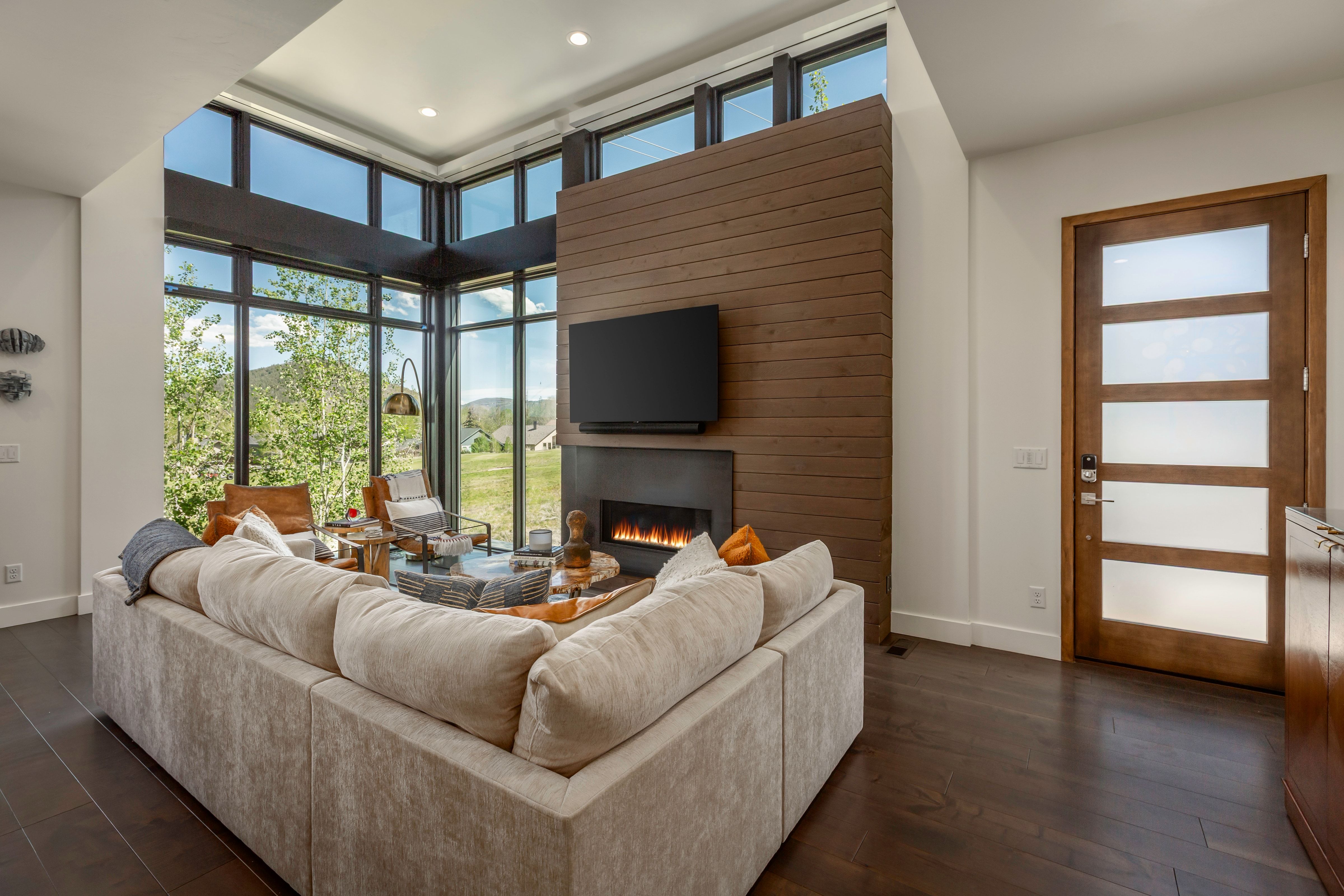 Living area featuring floor-to-ceiling windows, a wood-paneled accent wall with a mounted fireplace, and dark wood-finish flooring
