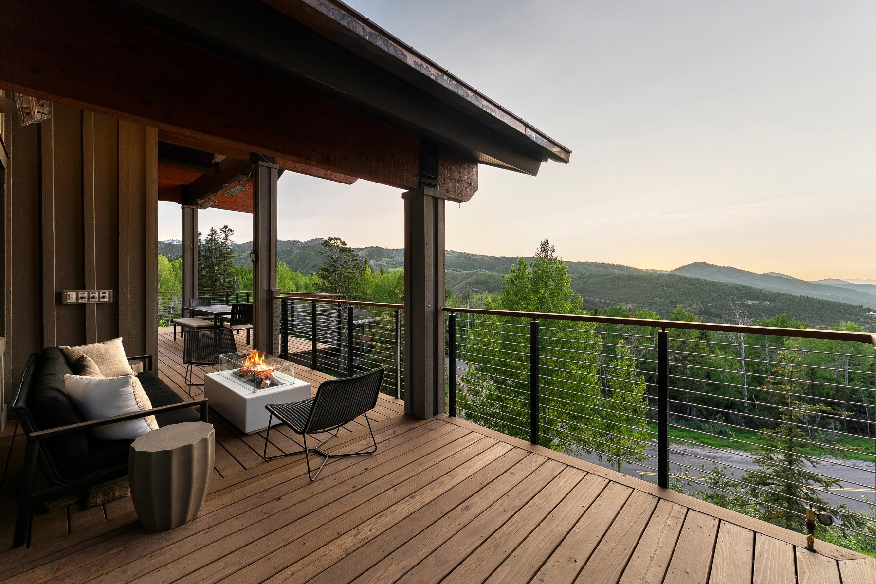 Expansive wooden deck featuring horizontal cable railing, a built-in fire pit, and exposed structural beams