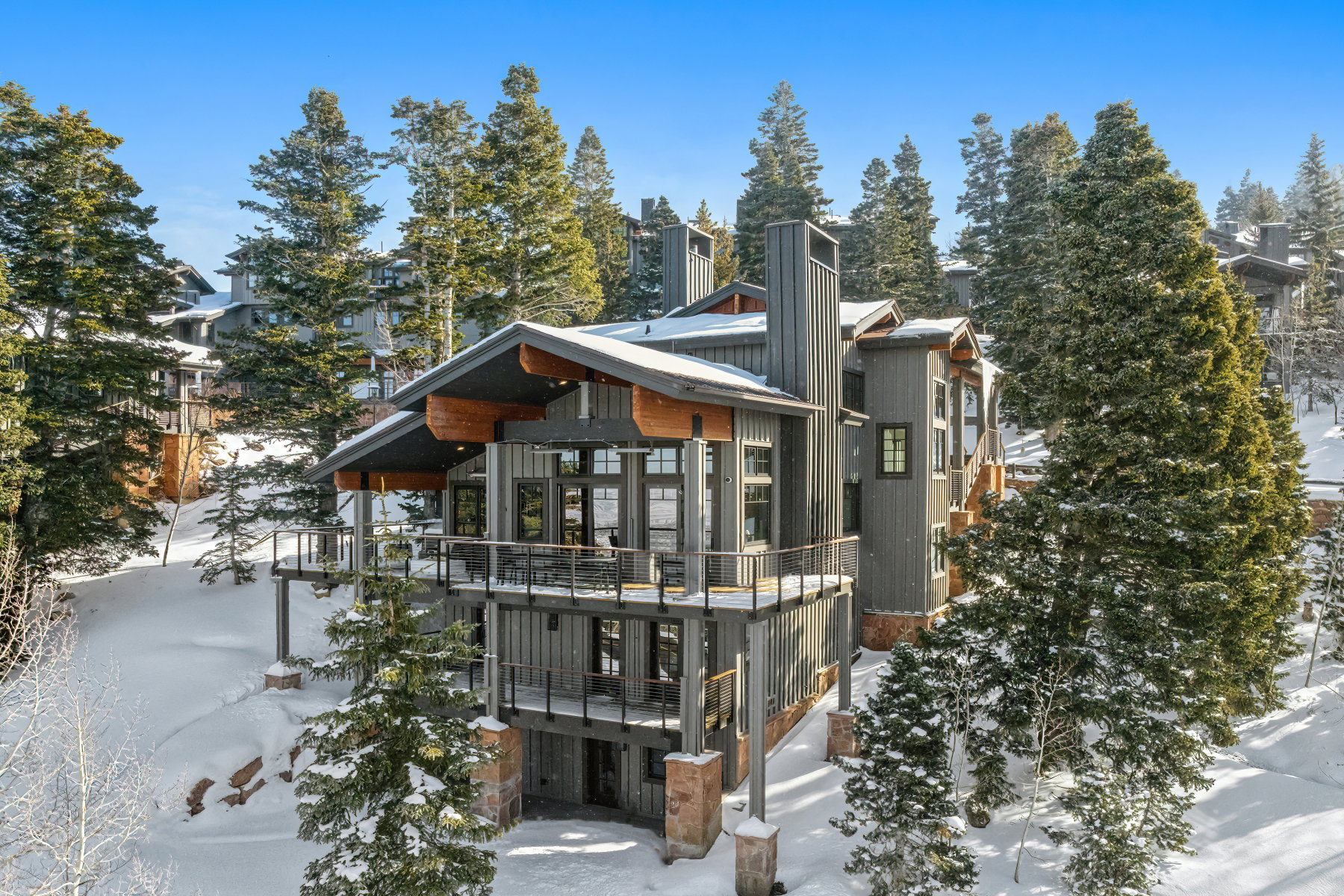 Multi-level residence featuring dark vertical siding, multiple balconies with dark railings, exposed wood structural elements, and a tall integrated chimney