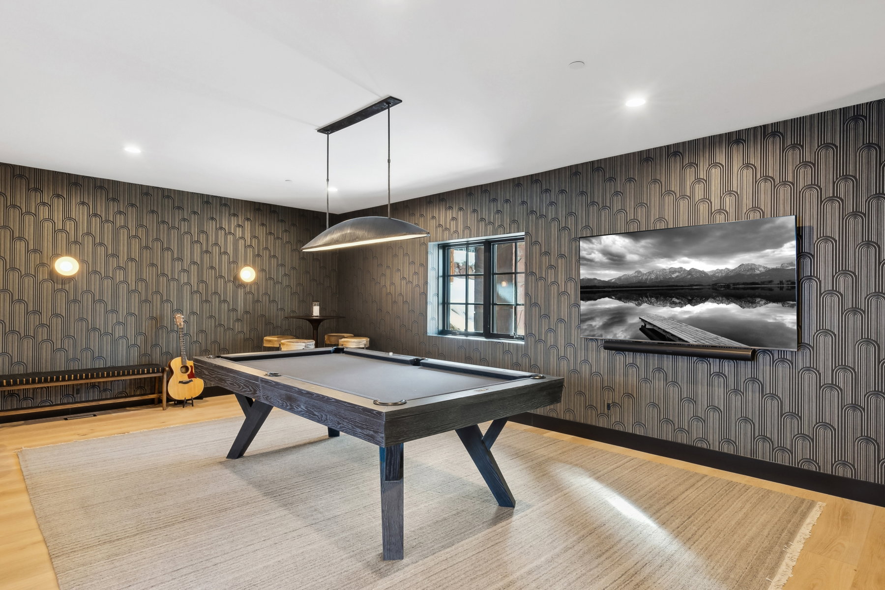 Recreation room featuring a modern pool table with dark wood-finish framing, light wood-finish flooring, patterned accent wall, and a large wall-mounted television
