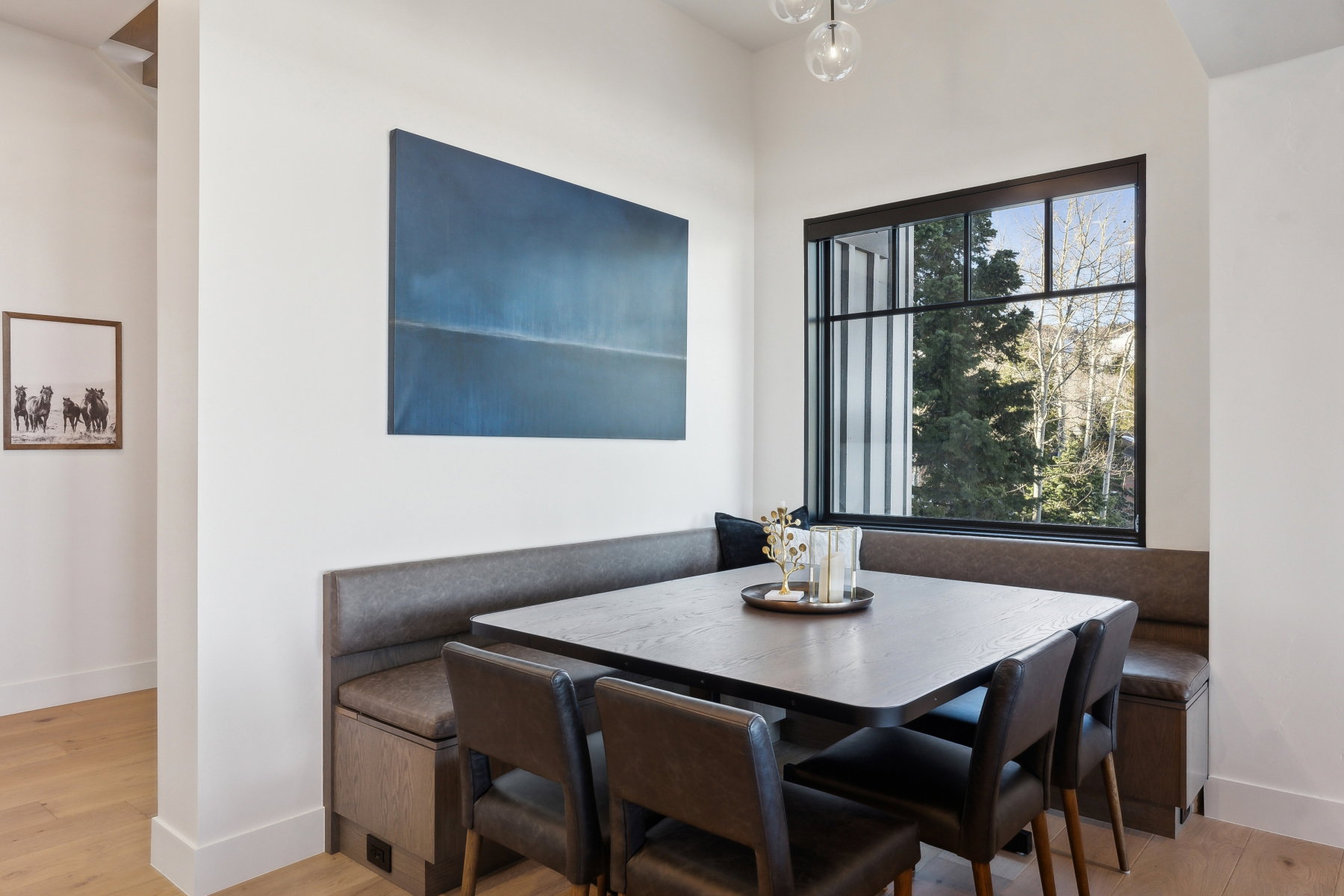 Built-in dining nook featuring upholstered bench seating with integrated storage, wood-finish flooring, and a large black-framed window