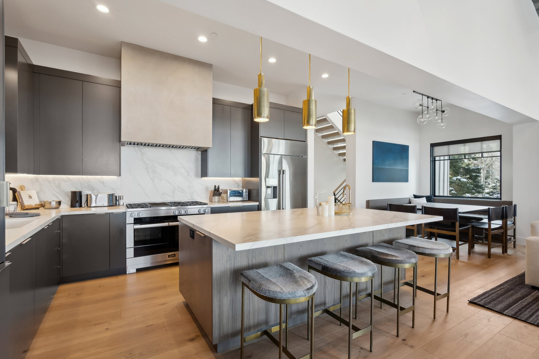 Modern kitchen featuring a large central island with seating, stainless steel appliances, a built-in range hood, dark cabinetry, and light wood-finish flooring