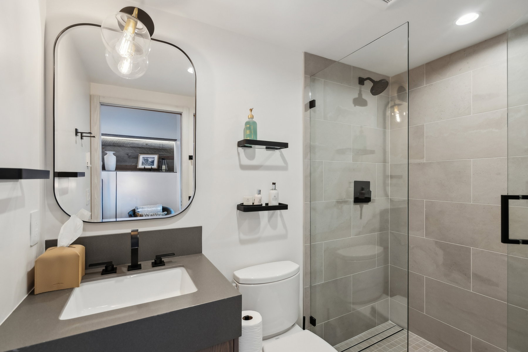 Bathroom featuring a rectangular sink with matte black fixtures, a wall-mounted mirror, and an enclosed shower with light-toned tiled walls and a glass door