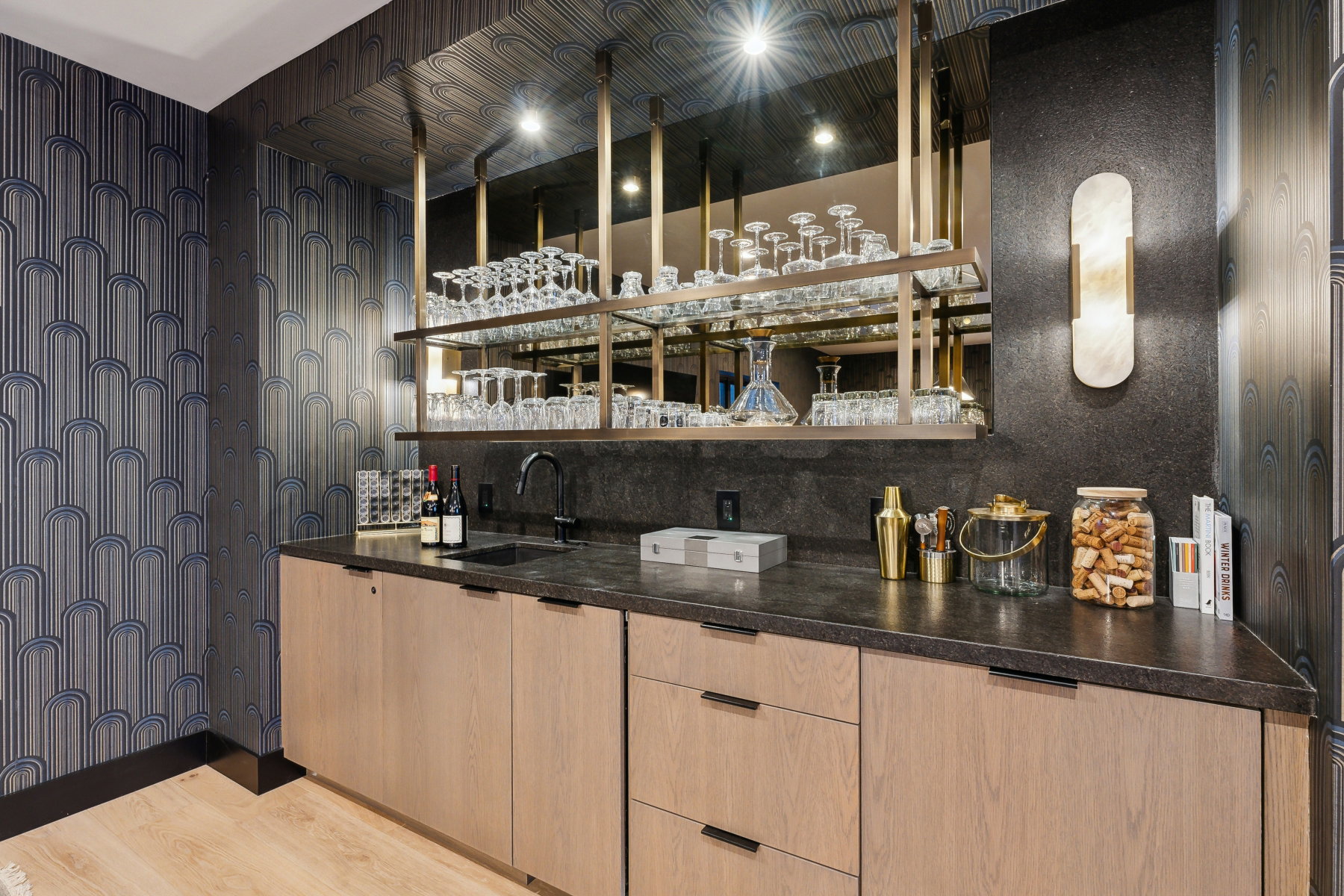 Built-in bar featuring wood-finish cabinetry, a dark stone countertop, integrated sink, and an elegant mirror backsplash