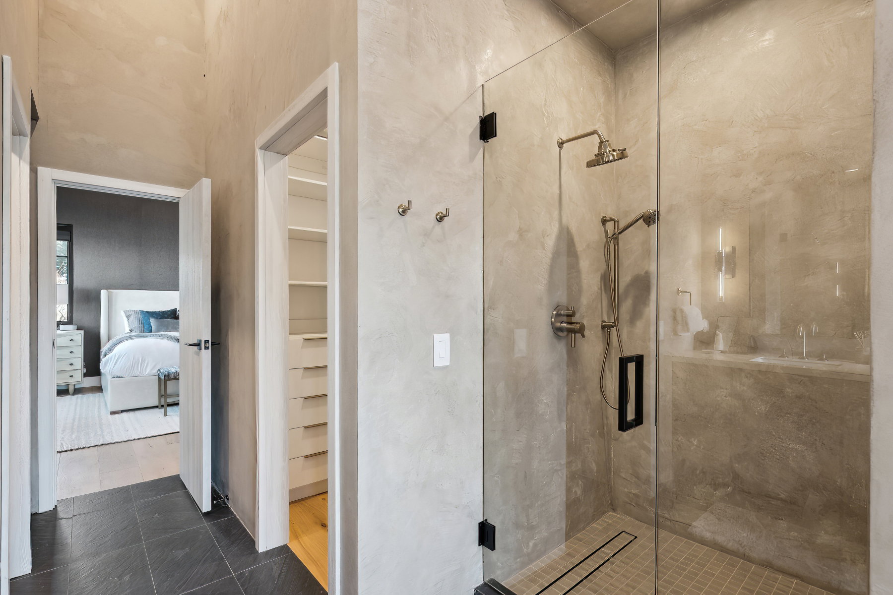 Glass-enclosed walk-in shower with dual shower heads, linear drain, and textured wall finish