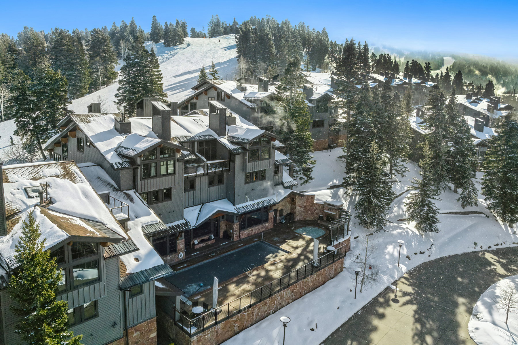 Mountain-style architecture featuring stone and wood siding, multiple balconies, a private hot tub, and an outdoor pool deck