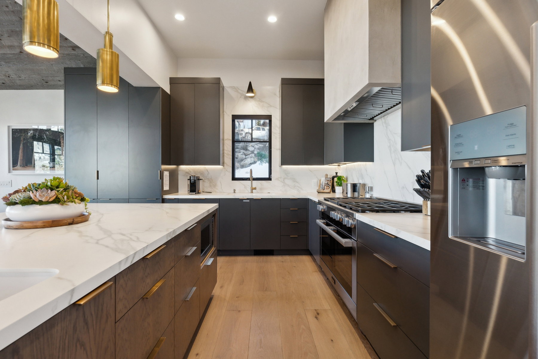 Gourmet kitchen featuring a large central island with a white stone countertop, a stainless steel refrigerator, dark wood-finish cabinetry, a stainless steel range, and light wood-finish flooring