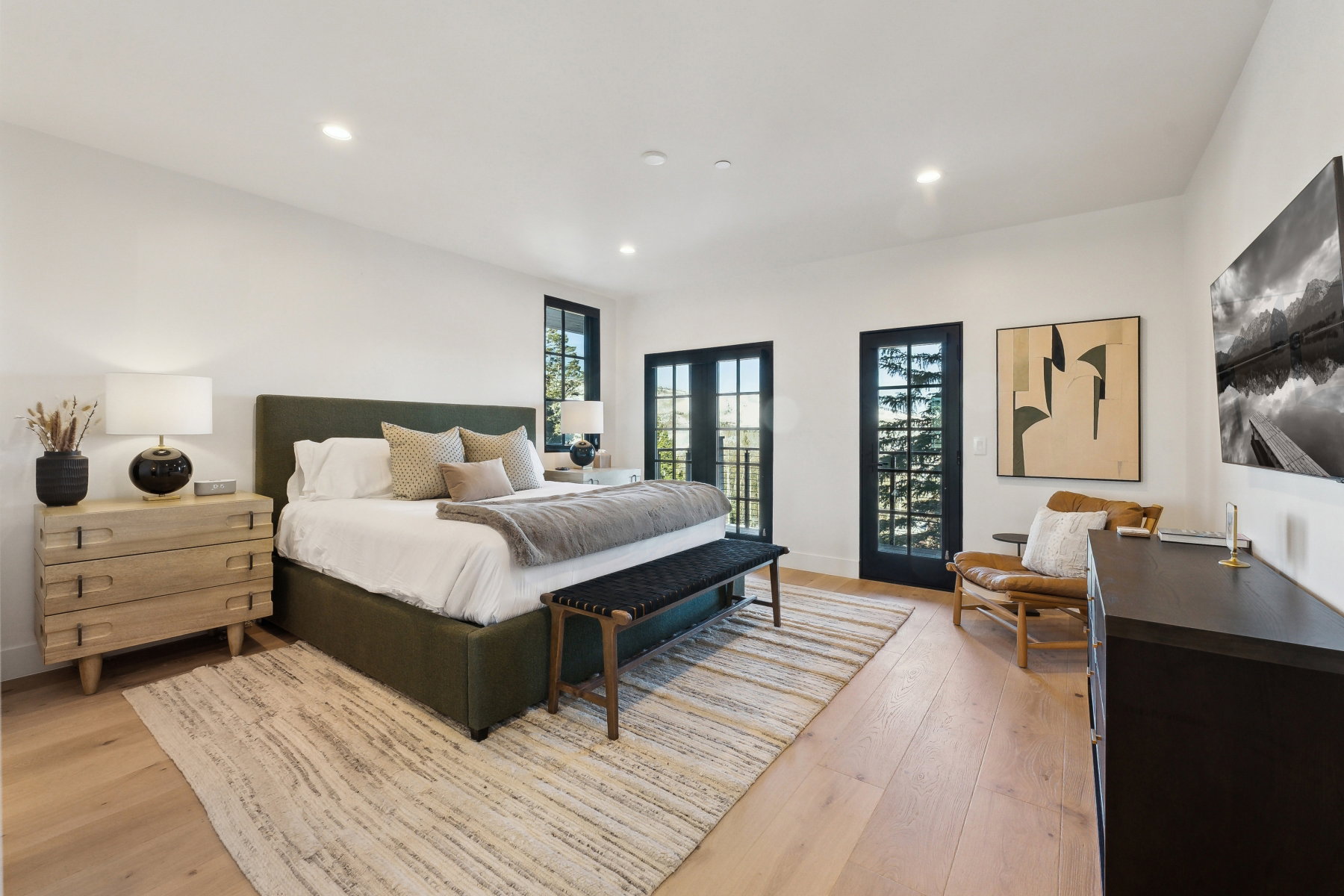 Spacious bedroom featuring light wood-finish flooring, recessed lighting, and two sets of French doors with black frames