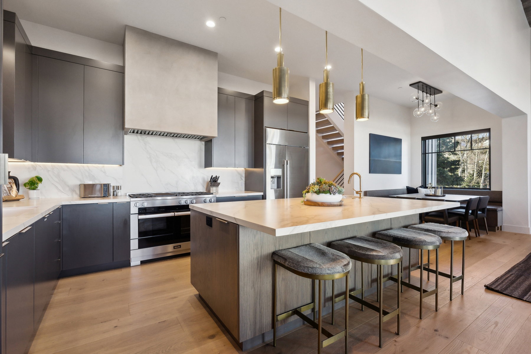 Gourmet kitchen featuring a large island with seating, stainless steel appliances, dark flat-panel cabinetry, light wood-finish flooring, and a dining nook with built-in bench seating