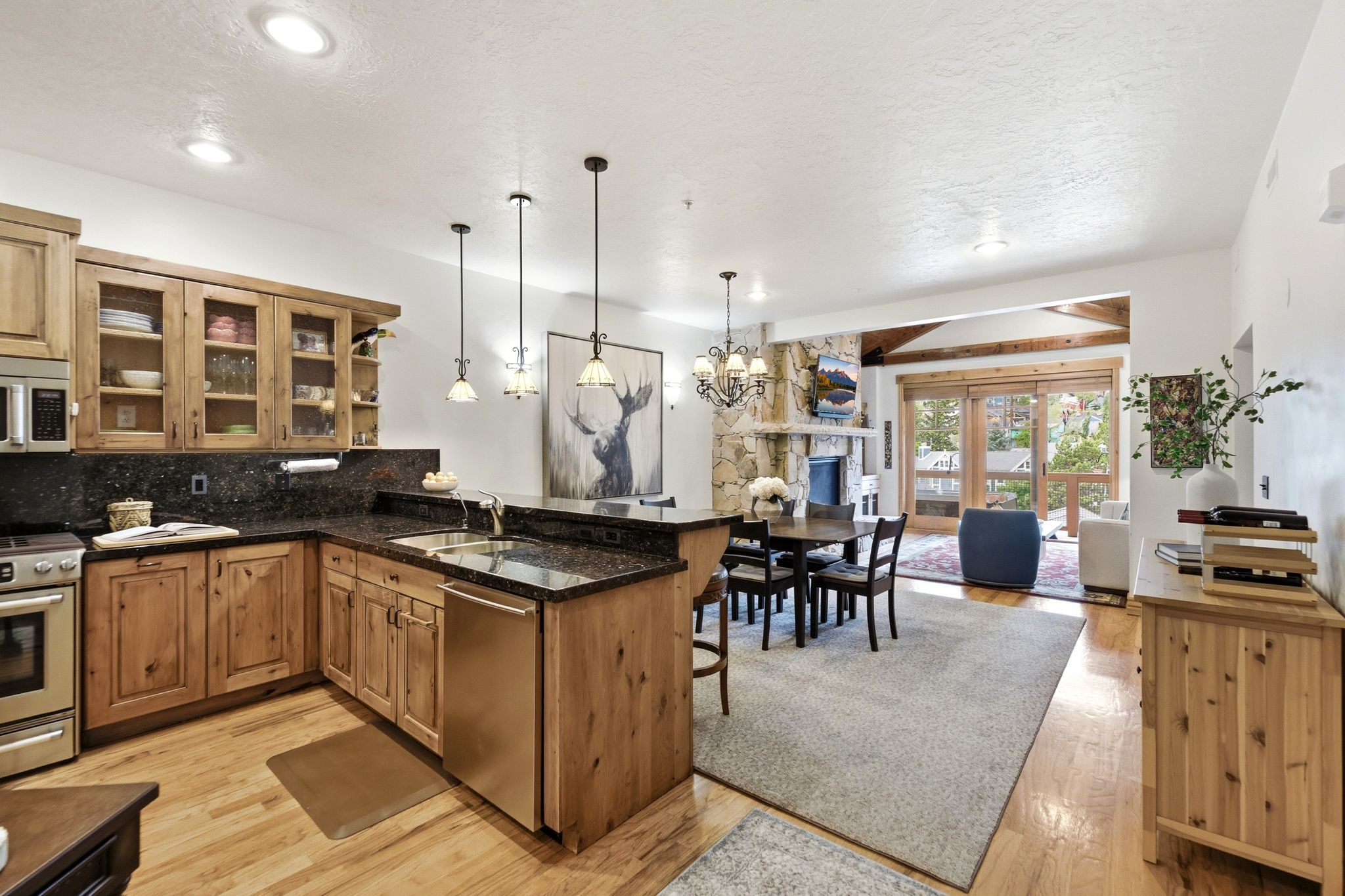 Open-concept kitchen and dining area featuring light wood cabinetry, granite, stainless steel appliances, and wood flooring